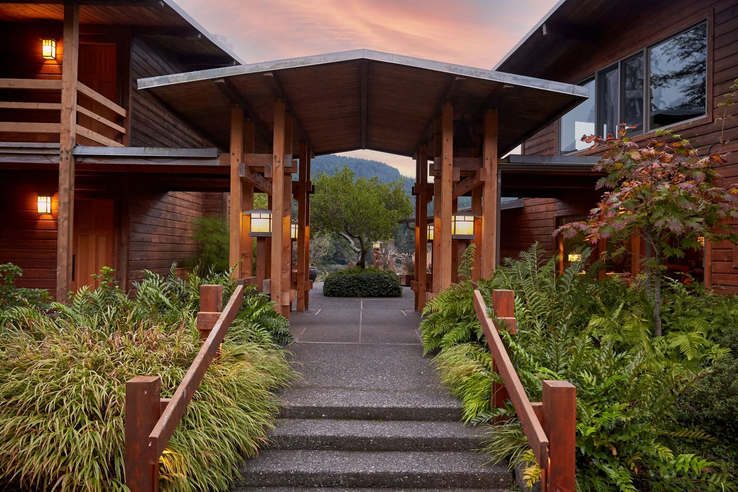 Stone pathway leading to wooden entrance with landscaped gardens and mountain views at dusk.