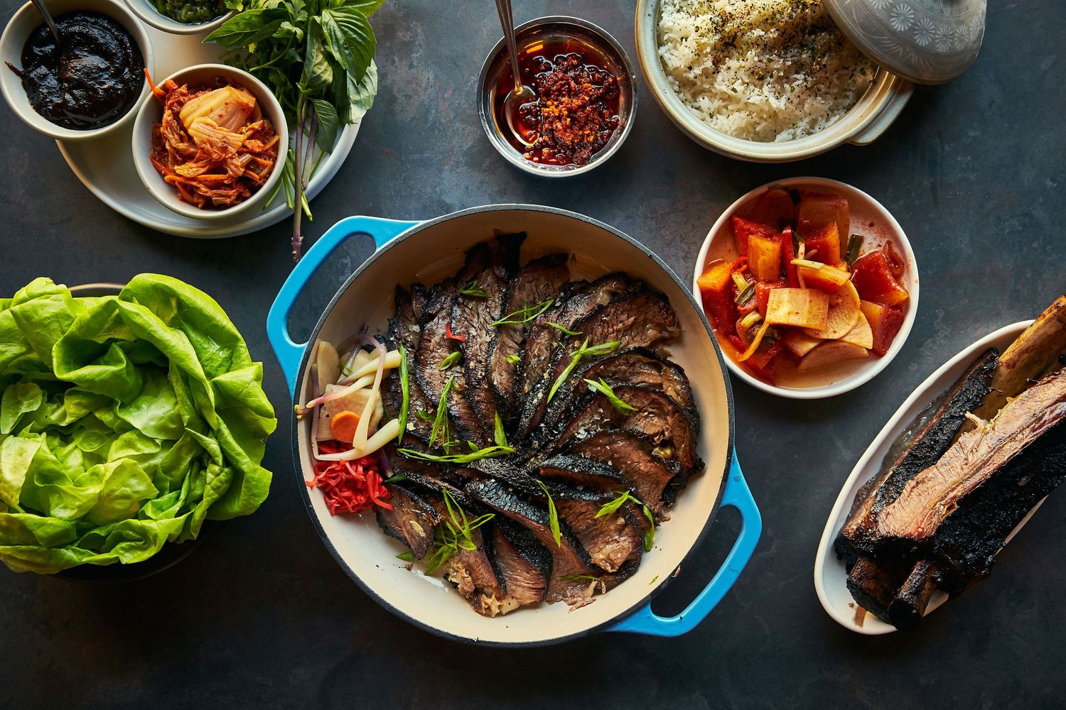 Assorted Korean BBQ dishes and banchan side dishes displayed on a dark table.
