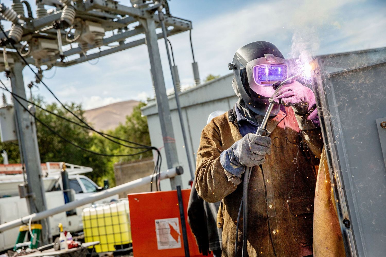 Welder in protective gear works with bright sparks flying in industrial setting.