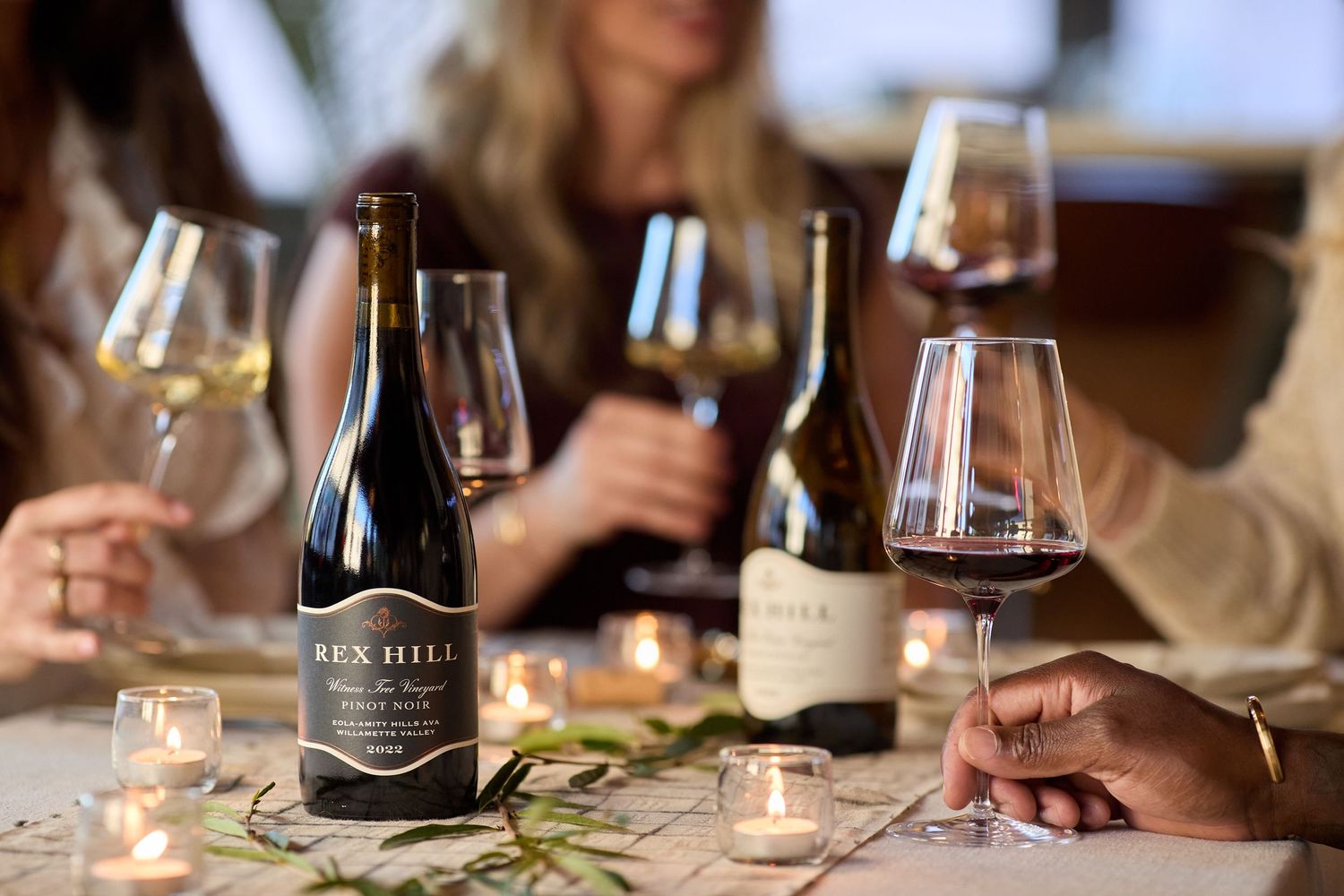 Wine tasting setup with multiple bottles and glasses on candlelit table.
