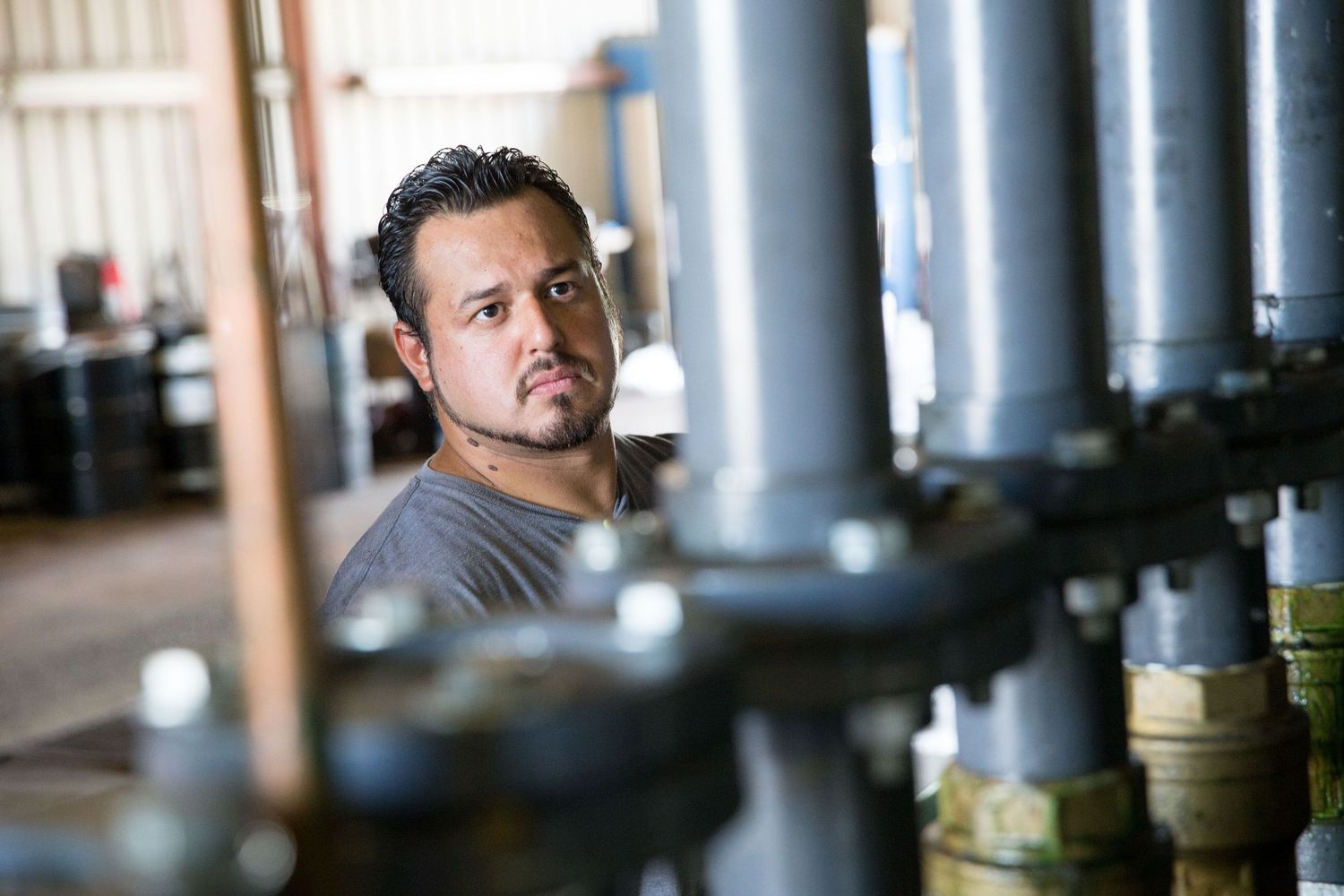 Worker monitors equipment among industrial pipes and machinery.