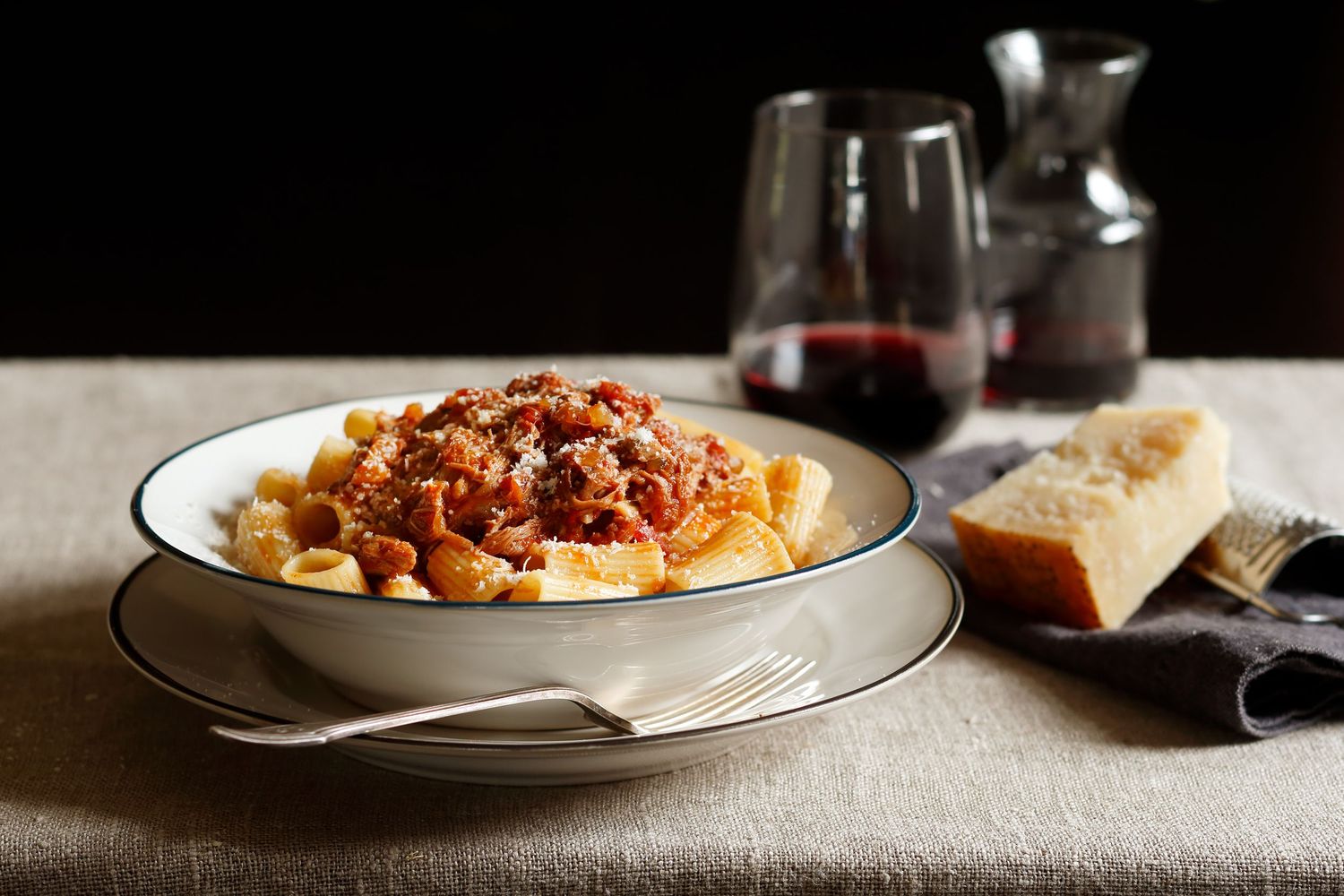 Rustic pasta dishes with sauce and garnishes served on white plates in moody lighting.