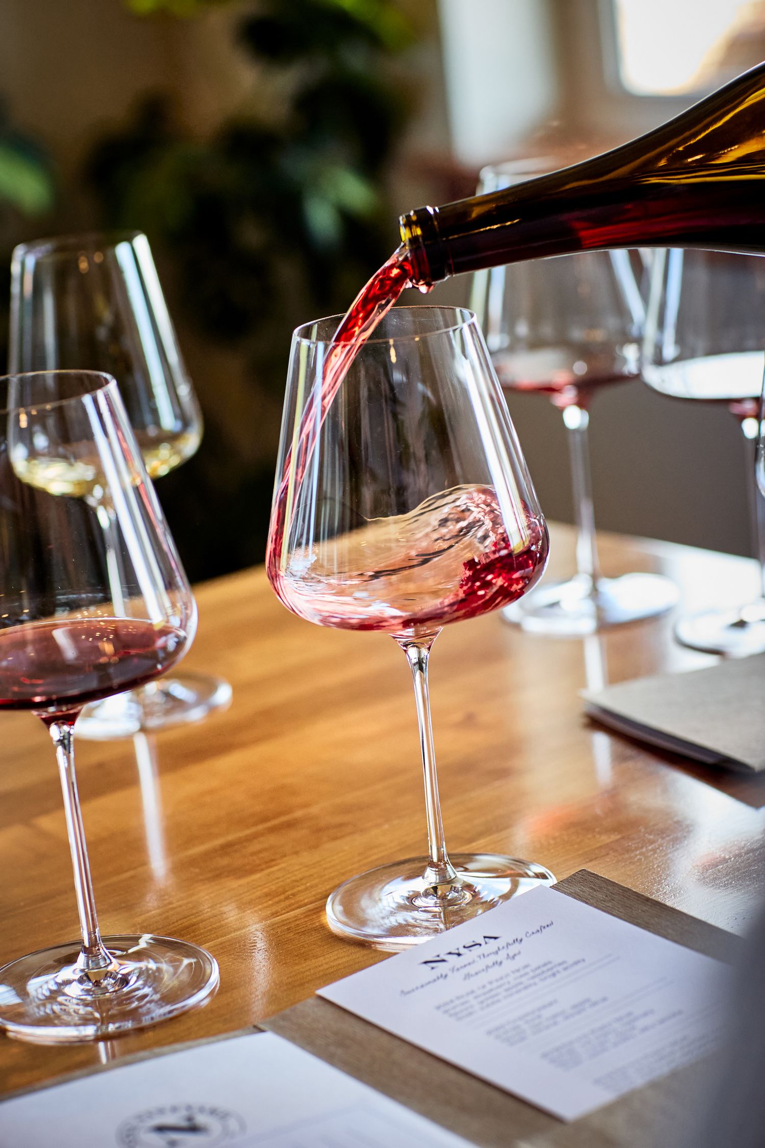 Red wine being poured into elegant wine glasses during a tasting with tasting notes on wooden table.