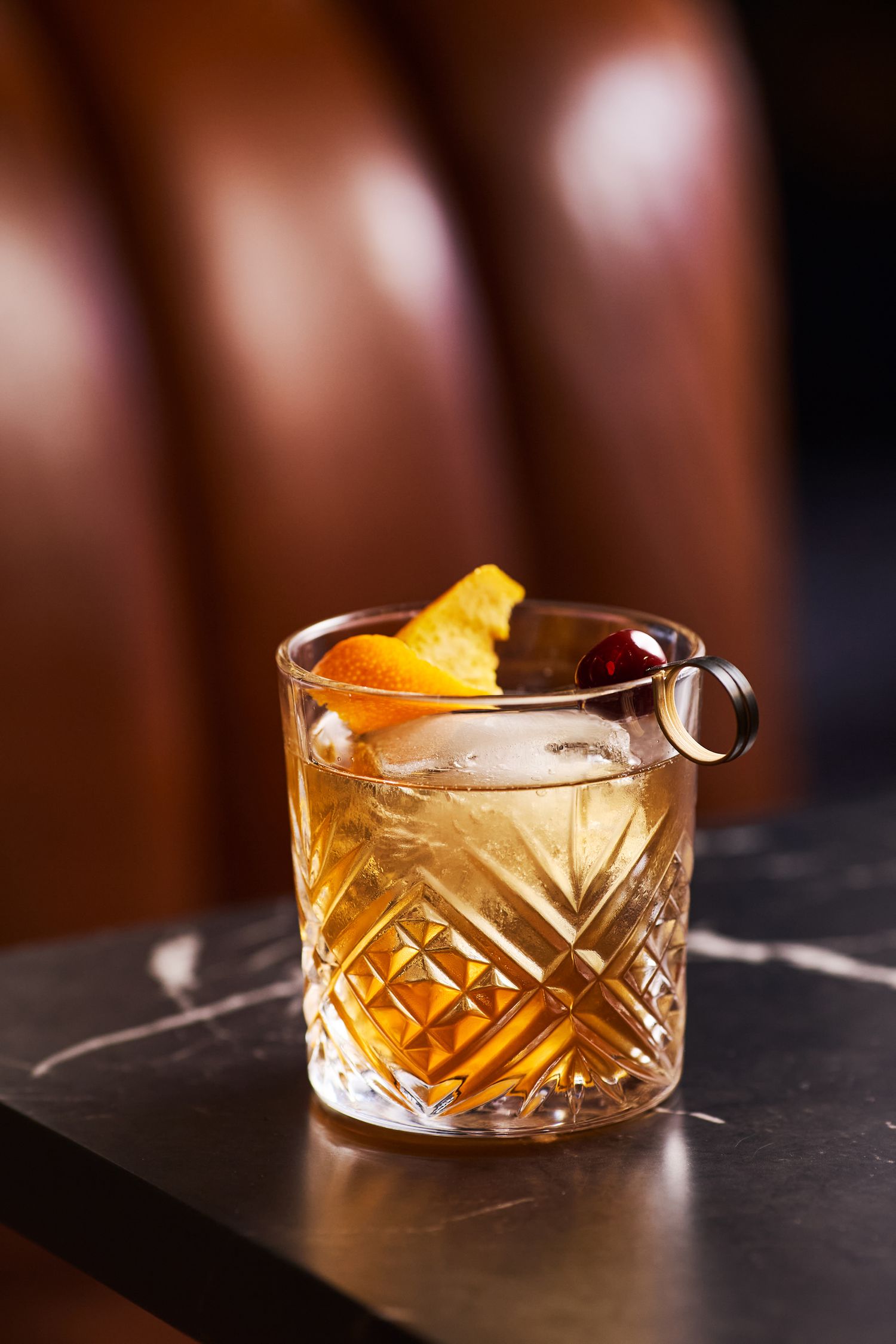 Elegant cocktail in a cut crystal glass garnished with an orange peel twist and dark garnish.