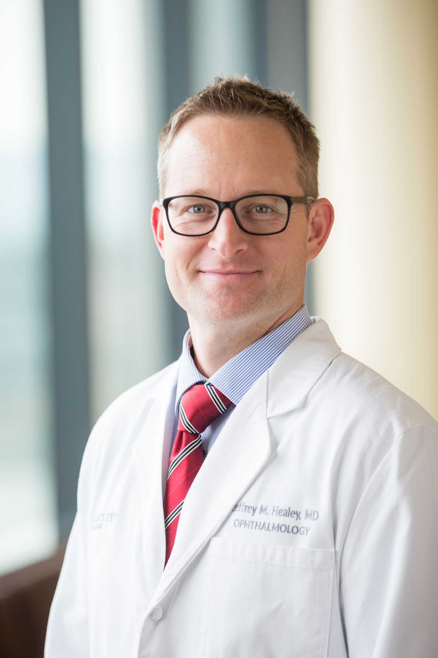 Medical professional in white coat and red tie standing in hospital corridor.