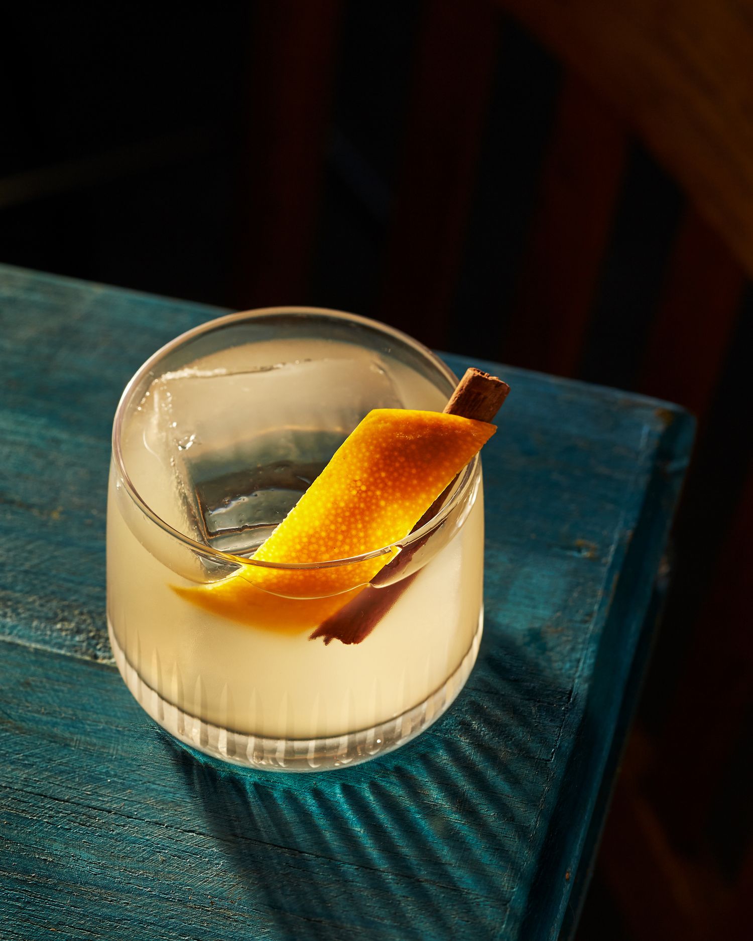 Craft cocktail with orange peel and cinnamon stick garnish in a coupe glass.