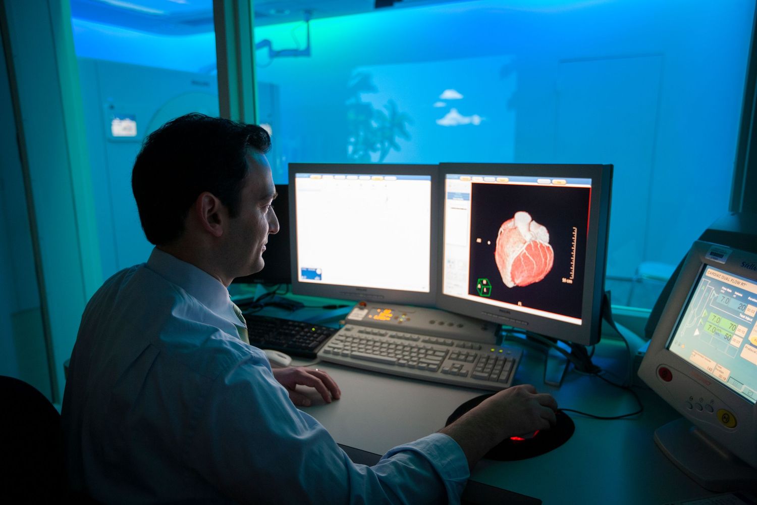 Medical professionals review brain scans and data on computer monitors in a dimly lit control room.