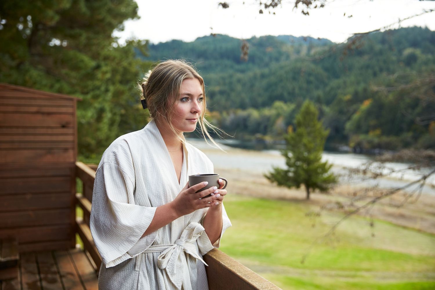 Person in white robe enjoying a drink on outdoor terrace with mountain views.