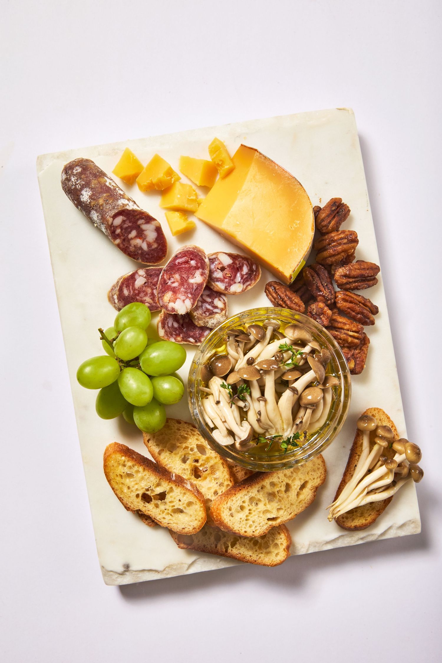 Charcuterie board with cheese, salami, grapes, nuts and marinated mushrooms.