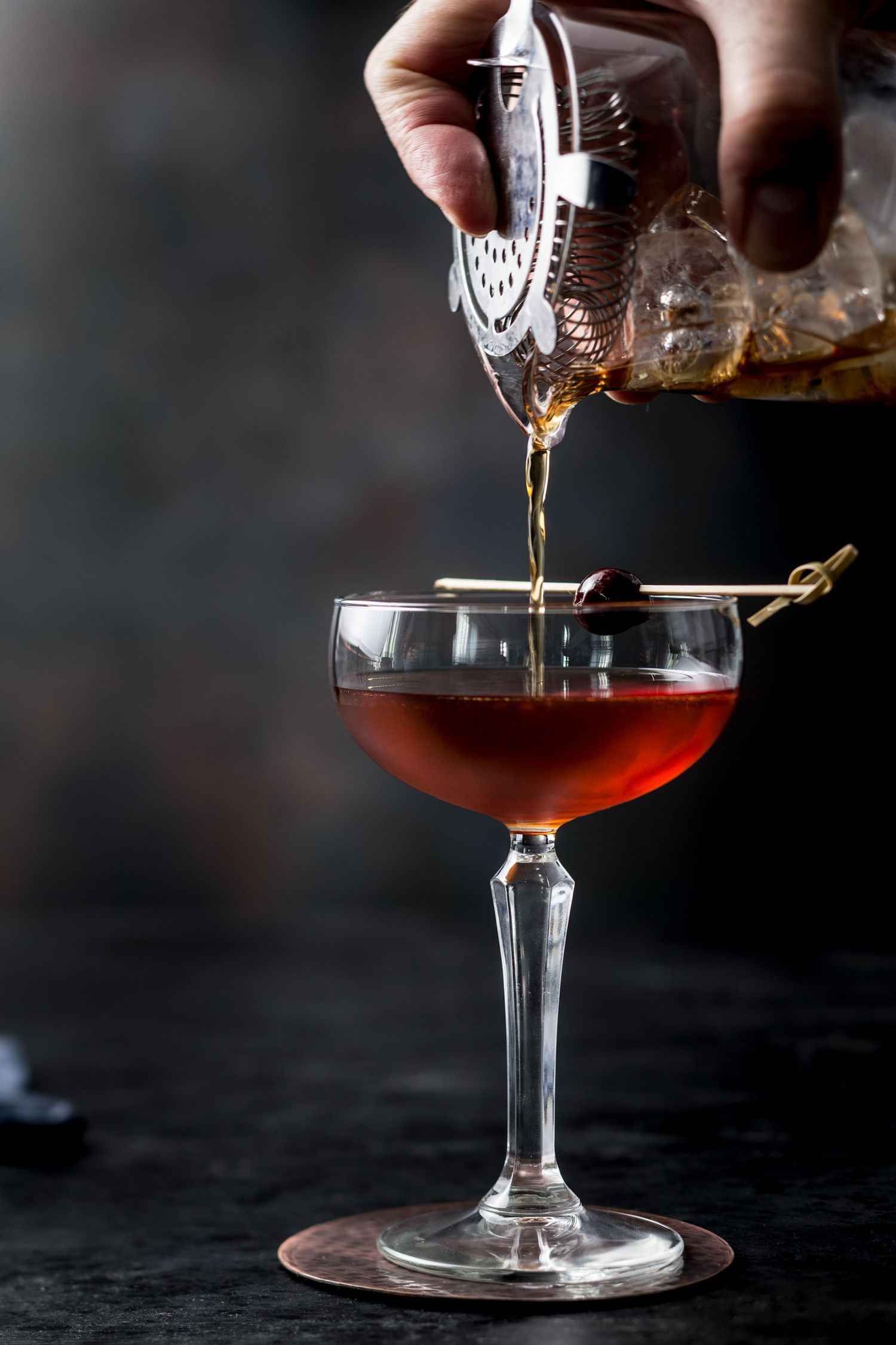 Dark amber cocktail being carefully poured into a stemmed glass.