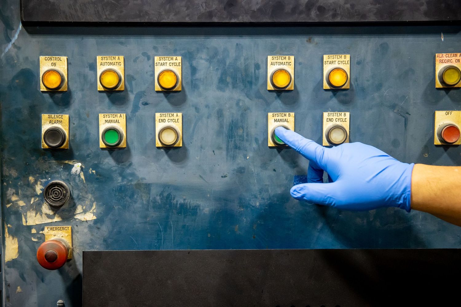 Row of control buttons and switches on industrial equipment panel with gloved hand.