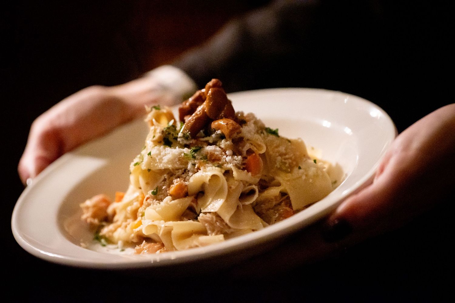 Elegant plated pasta dishes being served in white bowls on a wooden surface.