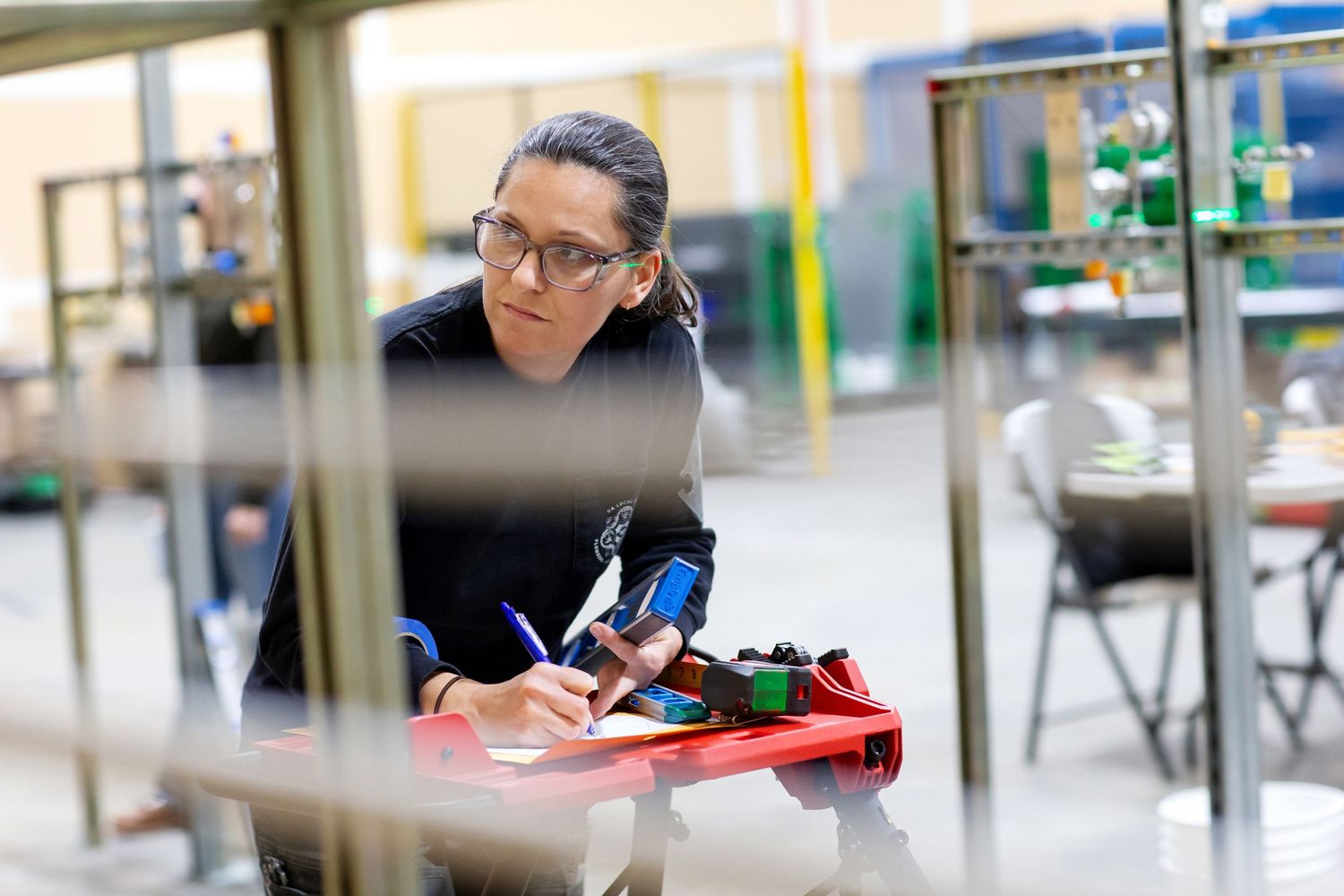 Person writing notes while examining technical equipment in industrial setting.