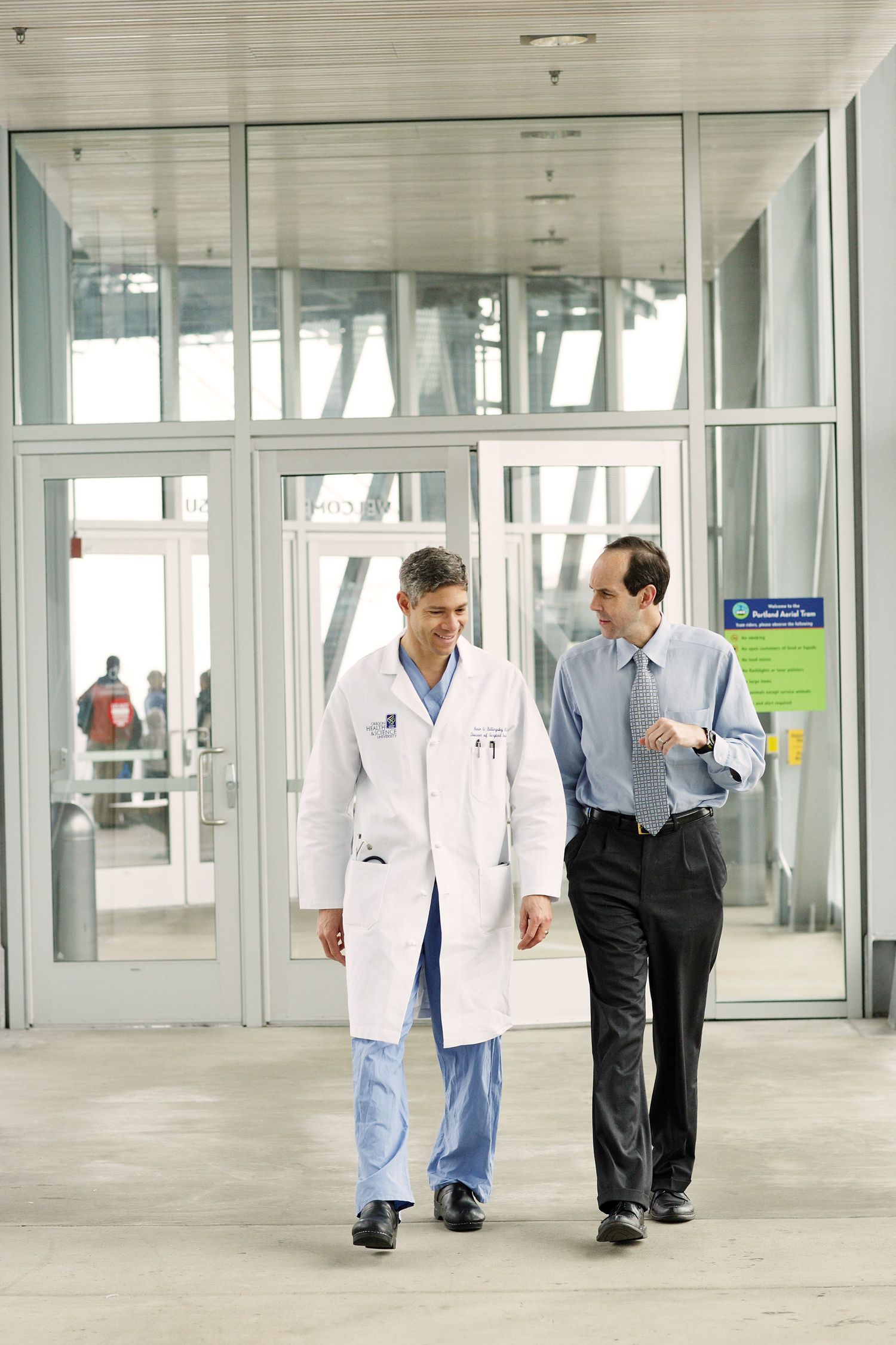Medical professional walking with colleague through modern hospital entrance.