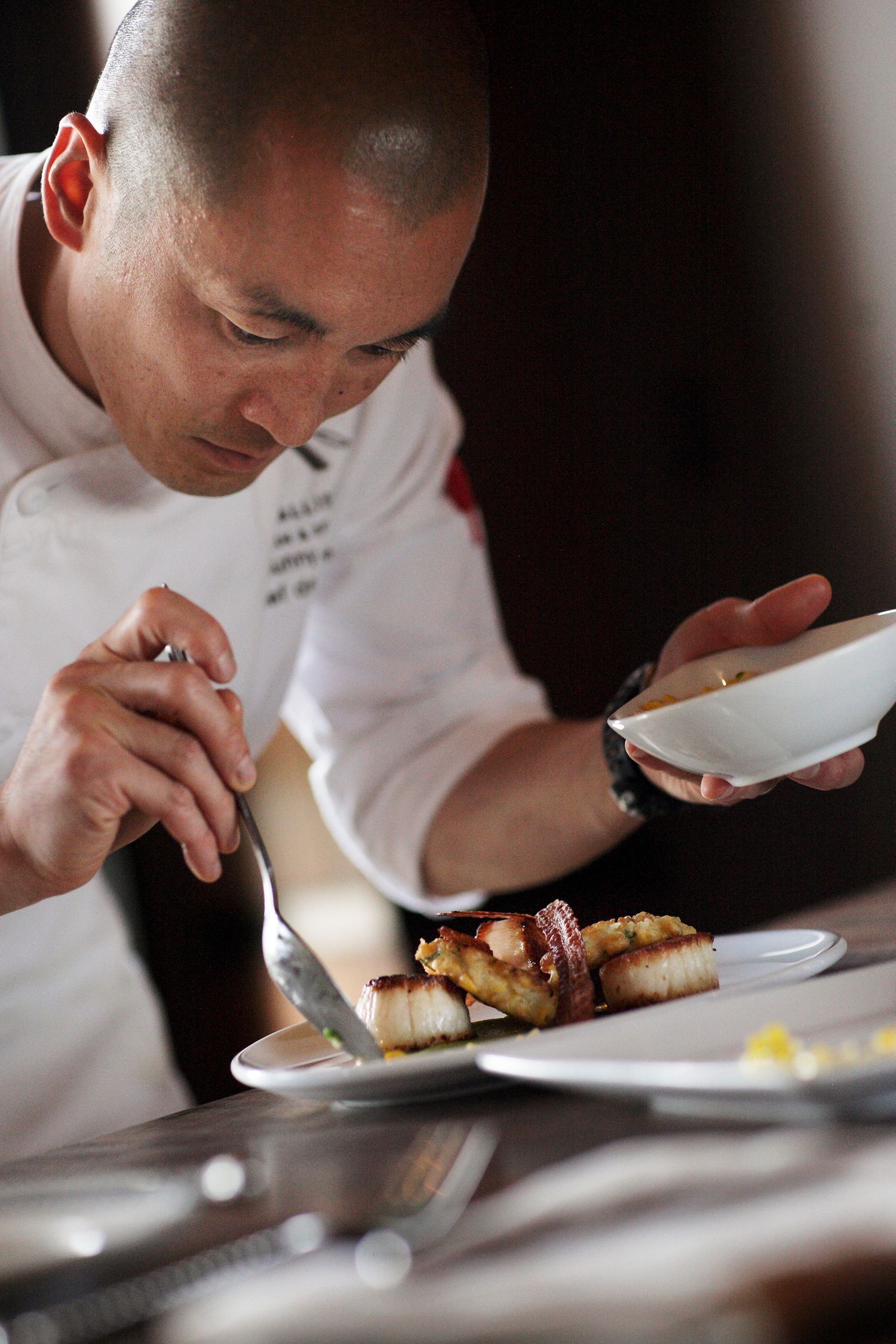 Chef carefully plating and inspecting fine dining dishes in restaurant kitchen.
