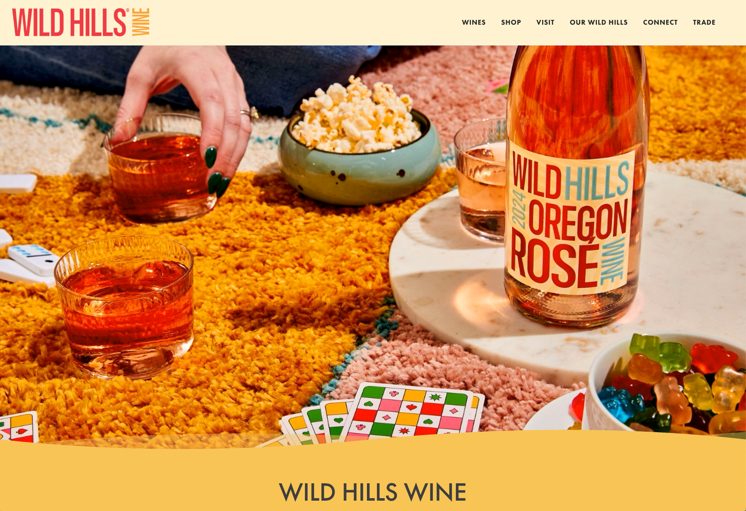 Bottle of Wild Hills Oregon Rosé wine on a table with cocktails, popcorn, gummy candy and playing cards on a bright orange shag rug.