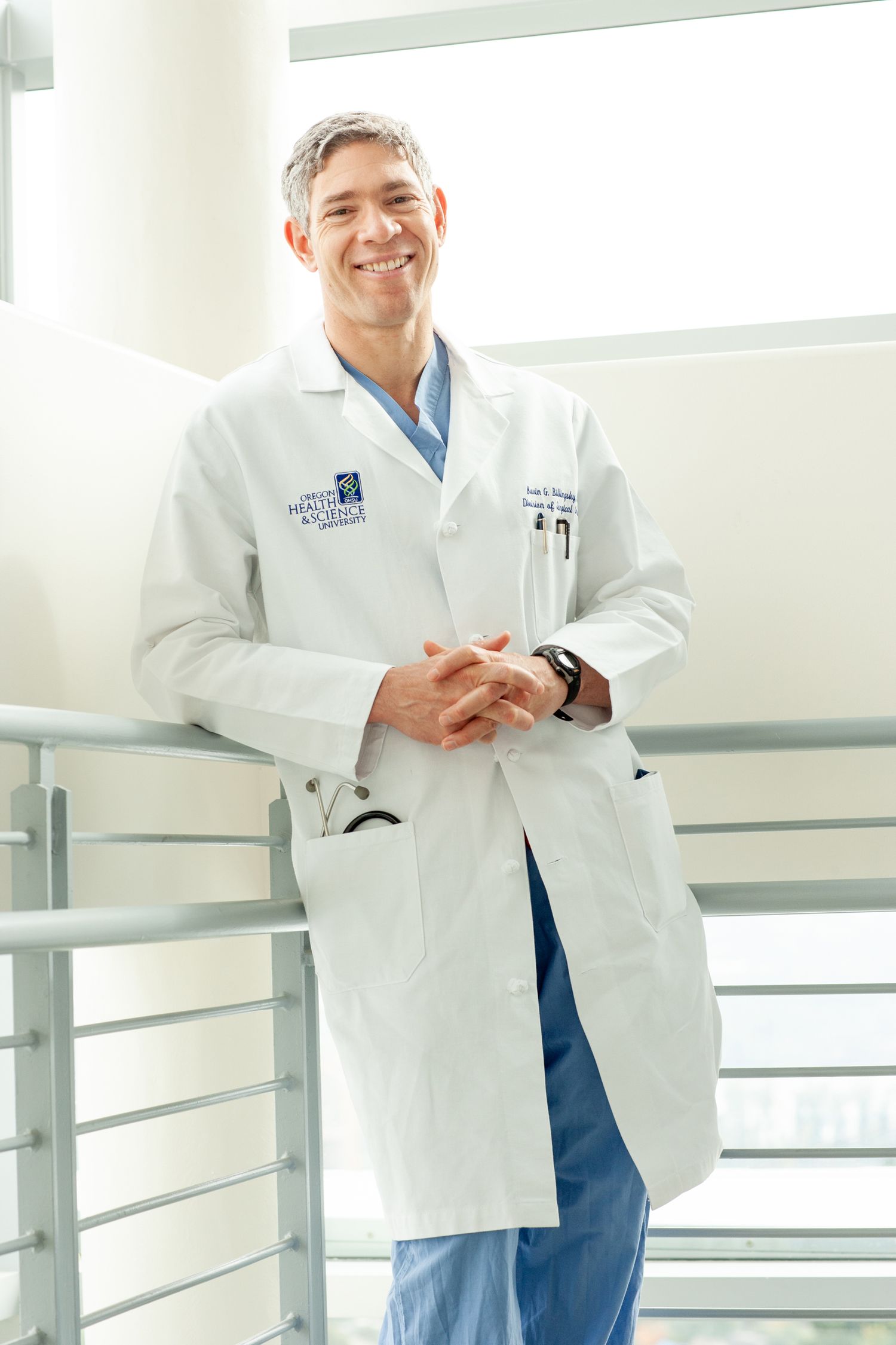 Healthcare professional in white coat standing confidently in bright medical hallway.