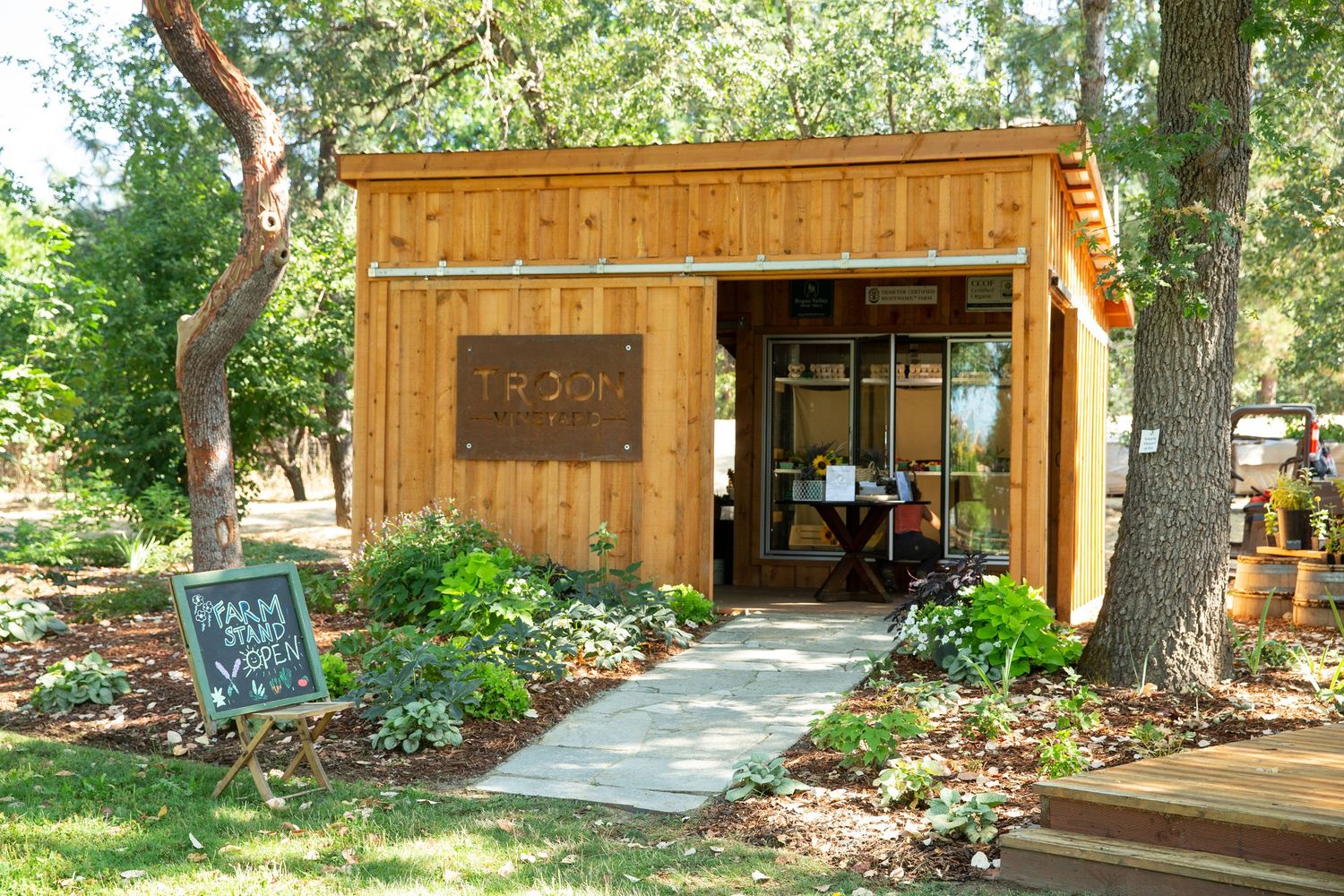A rustic wooden farm stand or shop exterior surrounded by green trees and foliage.