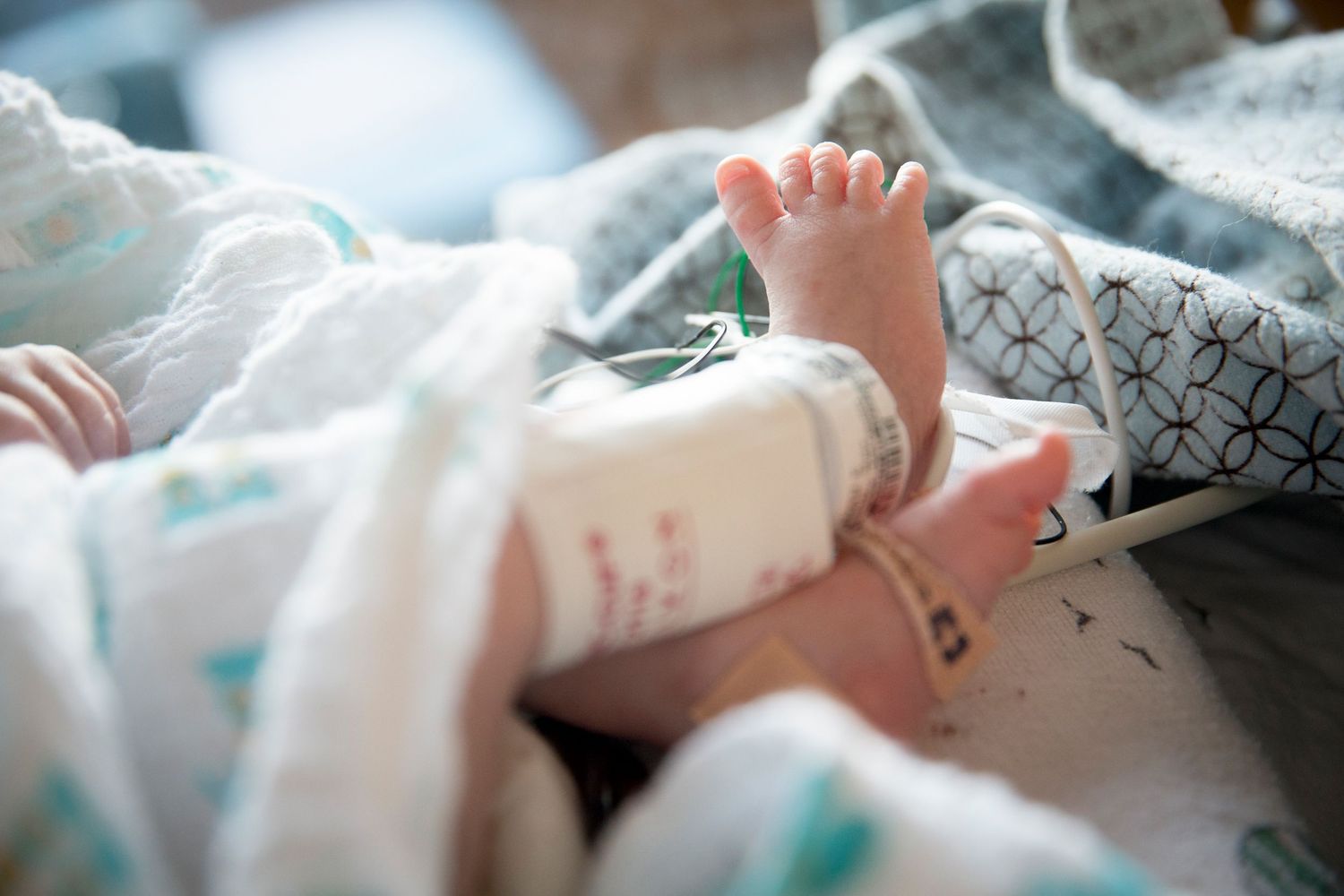 Tiny newborn baby feet wrapped in soft patterned hospital blankets.