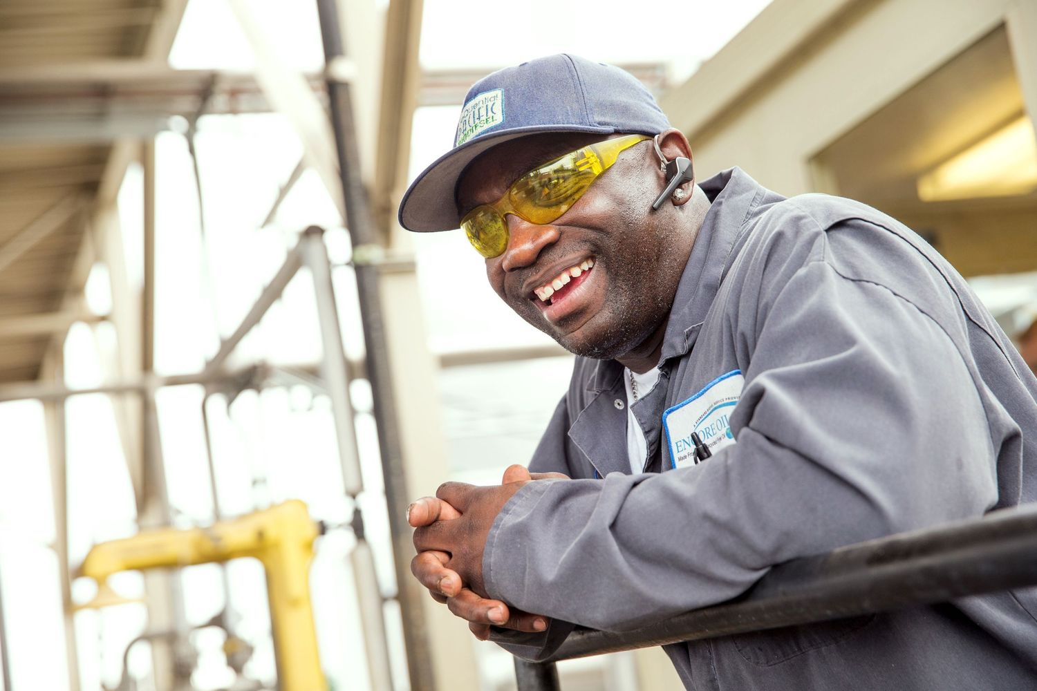 Industrial worker in safety gear and reflective sunglasses smiles while on the job.
