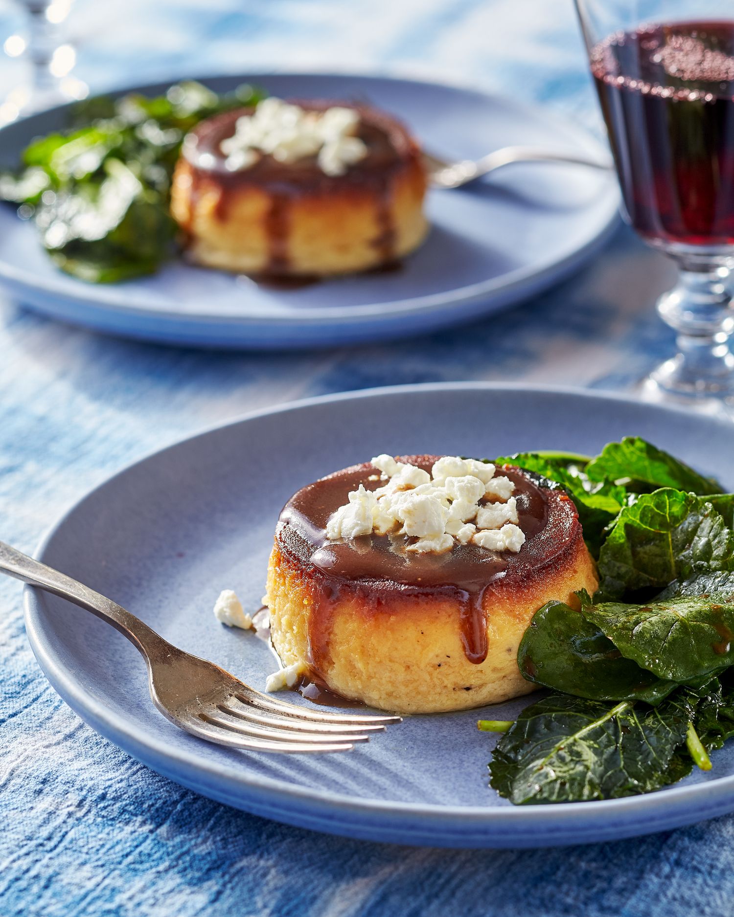 Golden flan desserts with caramel sauce served on blue plates with fresh greens.