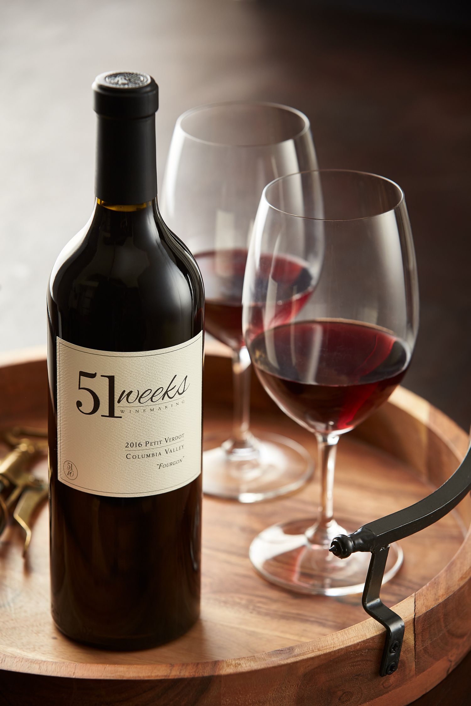 Wine bottle labeled '51 Weeks' with empty wine glasses on wooden serving board.