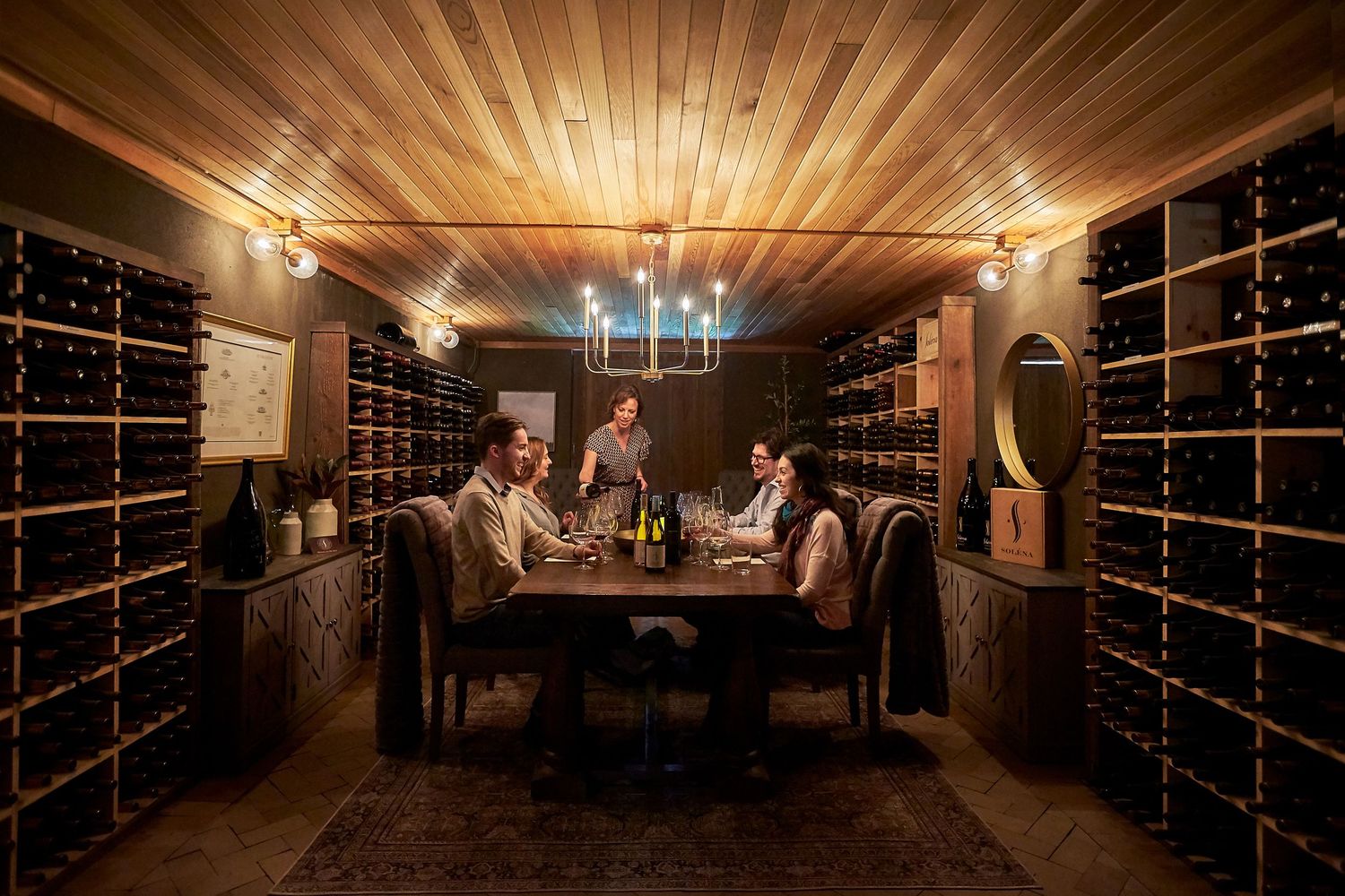 Wine cellar interior with wooden ceiling and rows of barrels lit by warm ambient lighting.