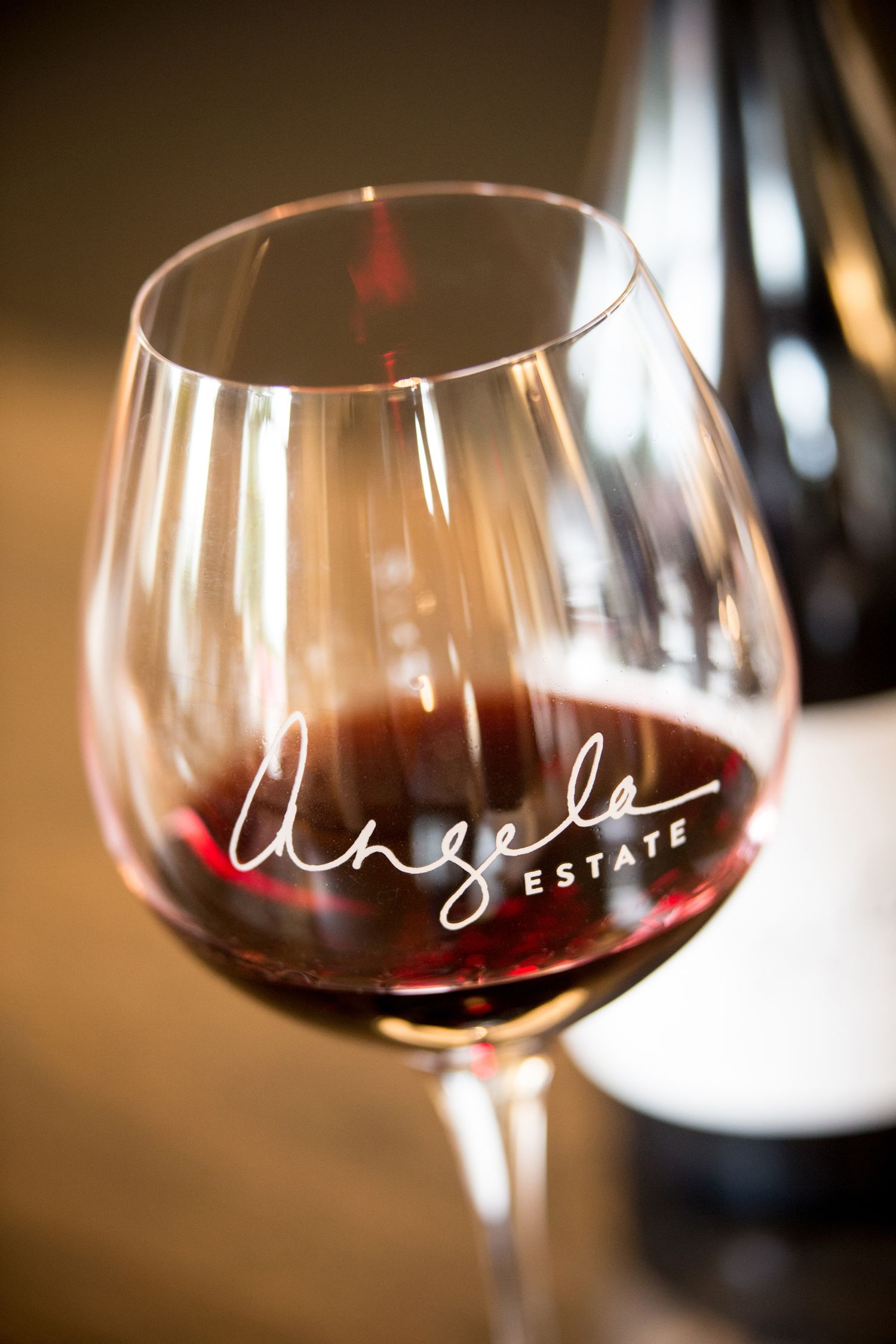 Close-up of wine glasses filled with red wine showing estate branding in soft focus.