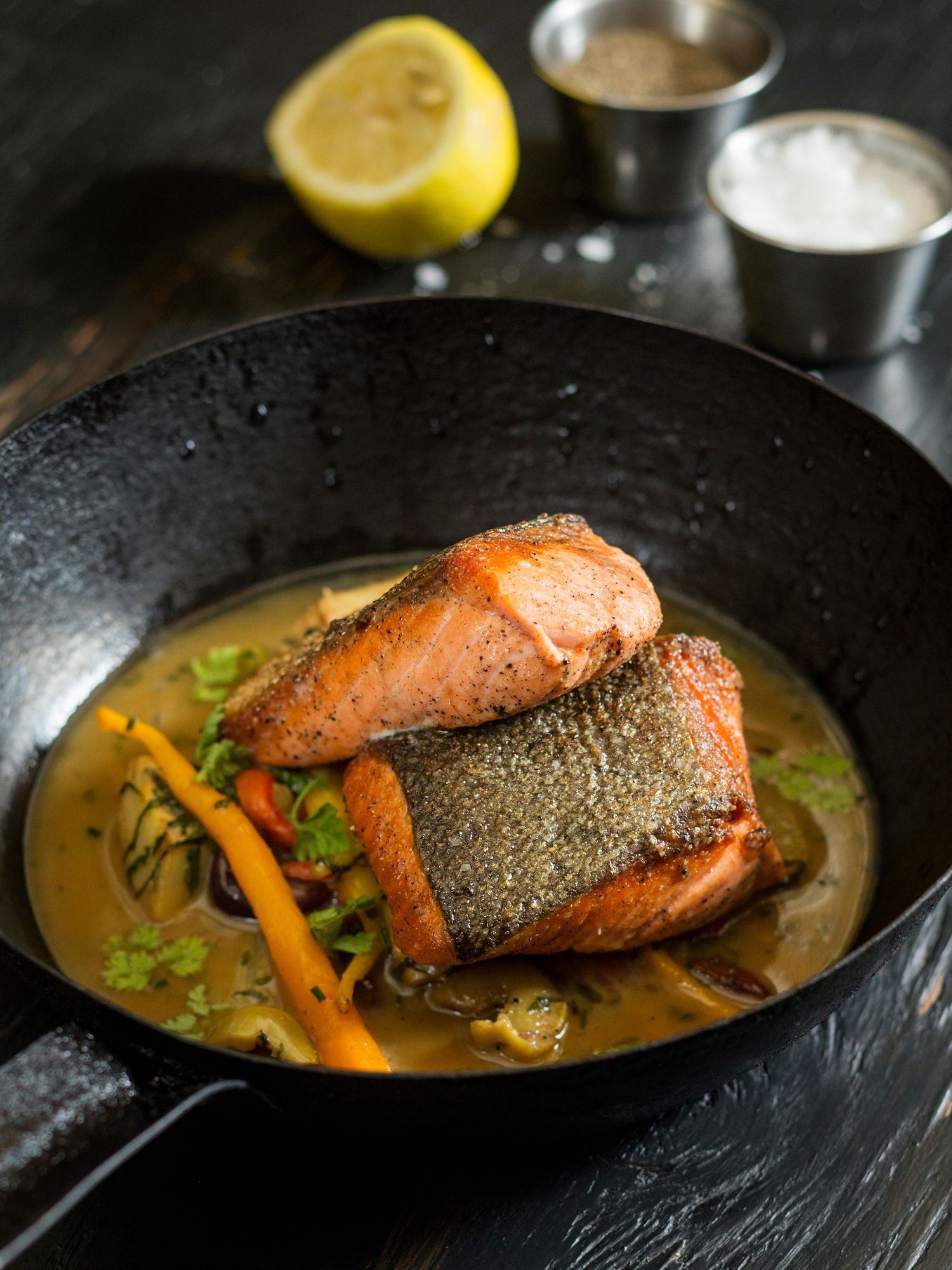 Pan-seared salmon fillet in a savory broth with colorful vegetables.