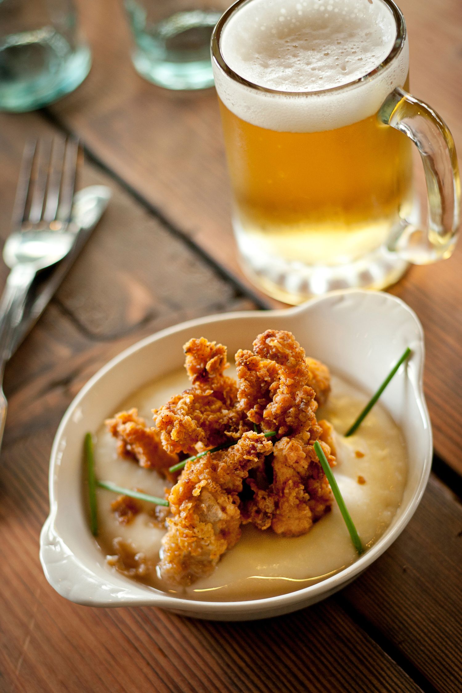 Crispy fried appetizers served on small white plates alongside golden beer in glass mugs.