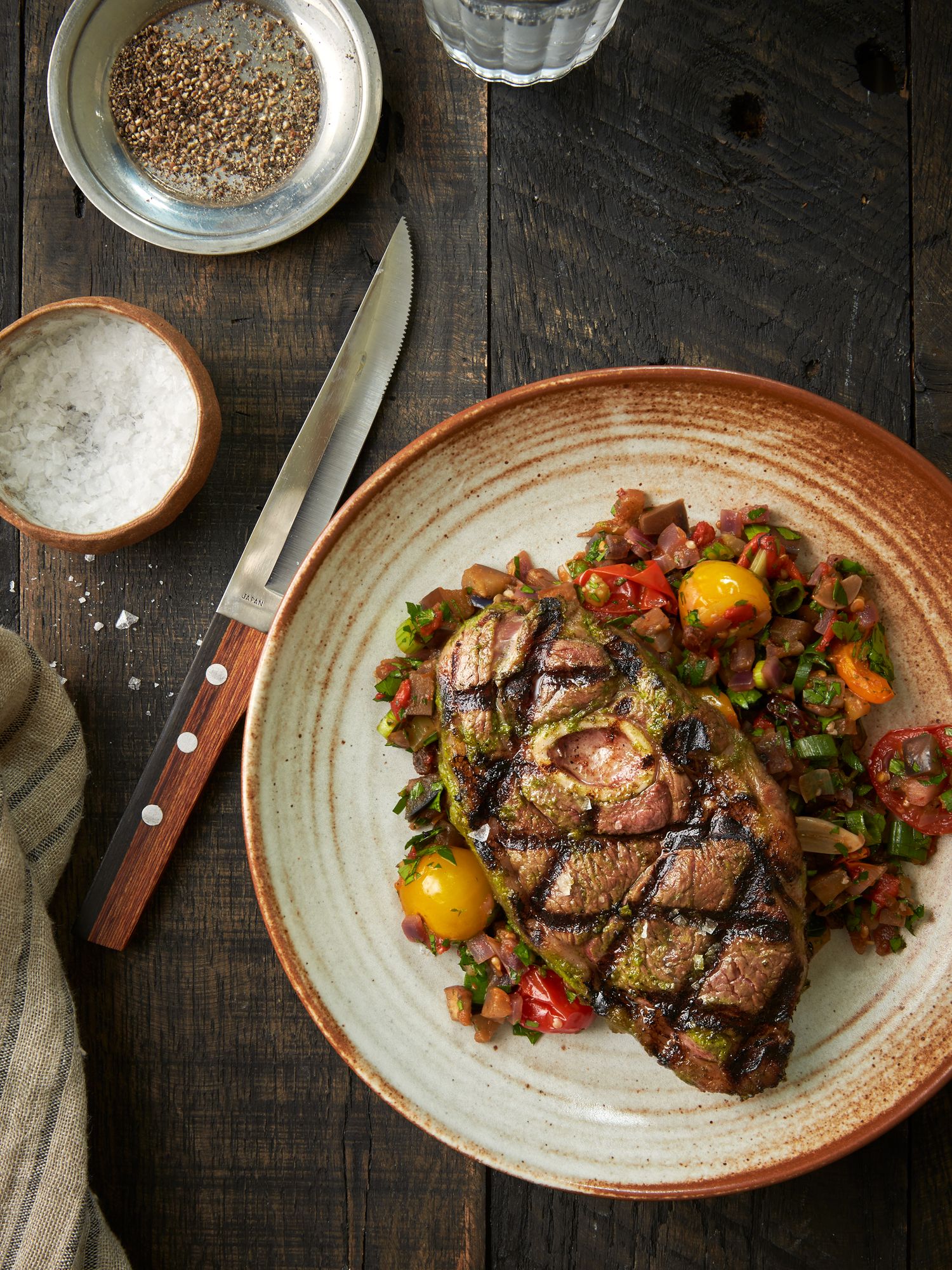Grilled steak topped with cherry tomatoes and vegetables on a rustic ceramic plate.