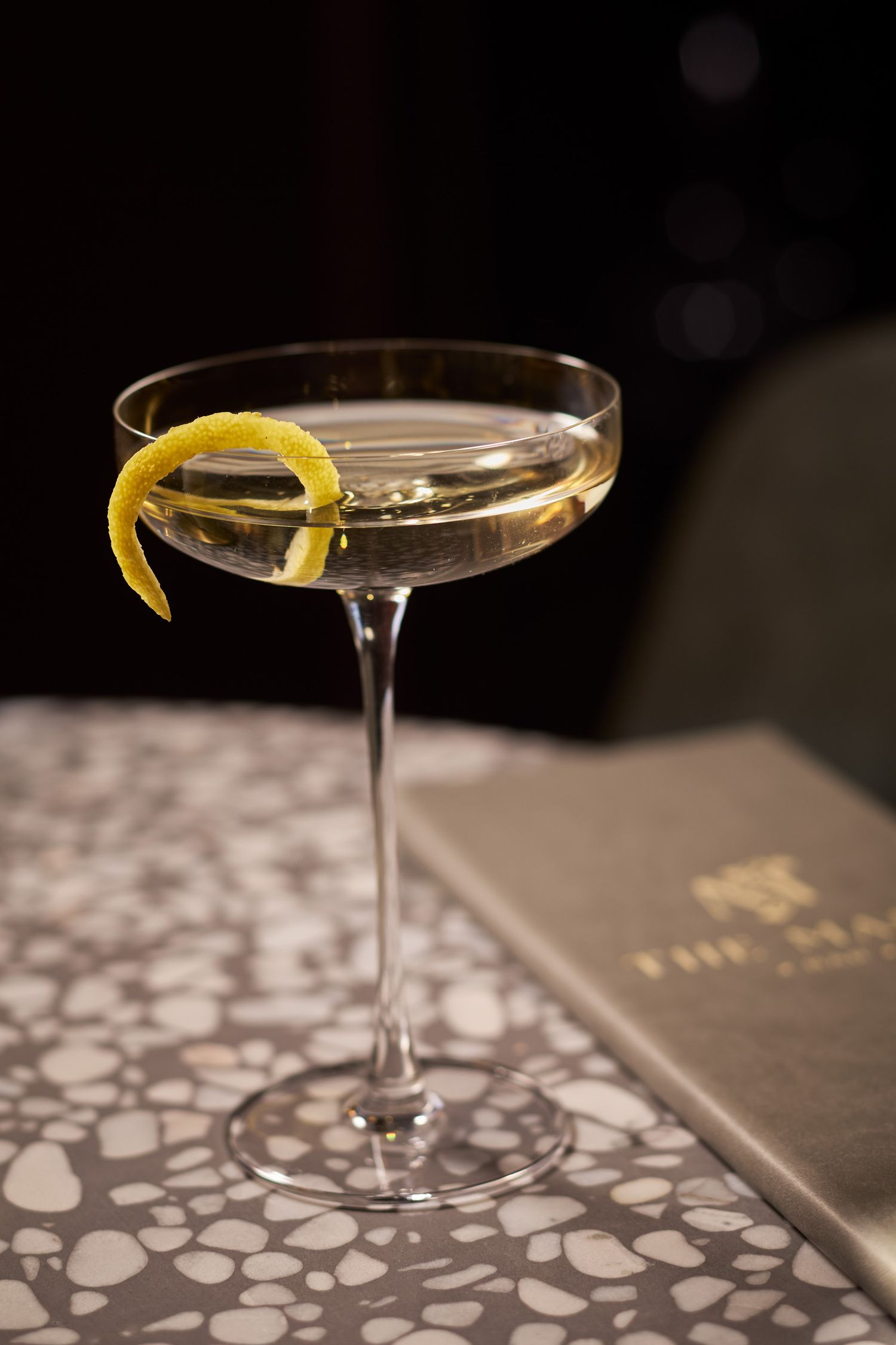 Martini cocktail with lemon twist garnish on a patterned table surface.