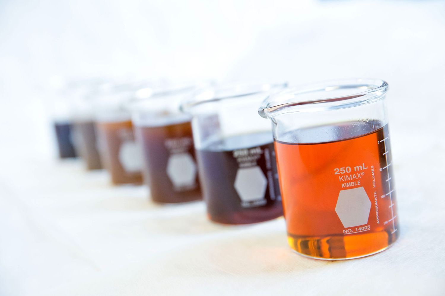 Row of orange liquid samples in glass vials lined up in laboratory setting.
