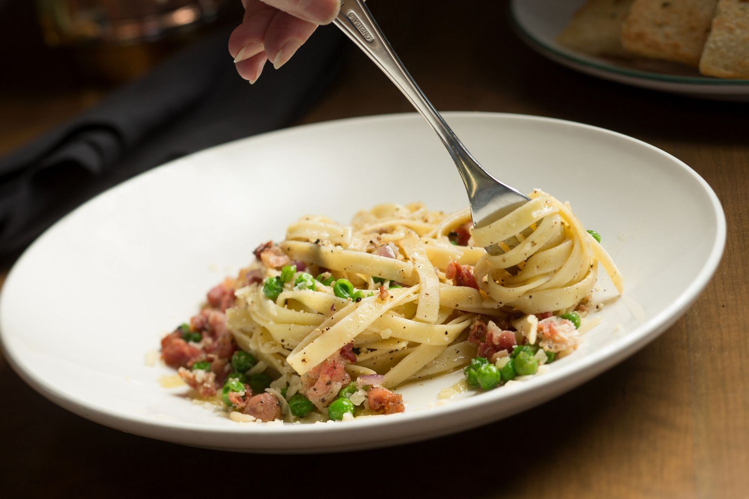 Creamy pasta carbonara with pancetta and parsley in a white bowl.