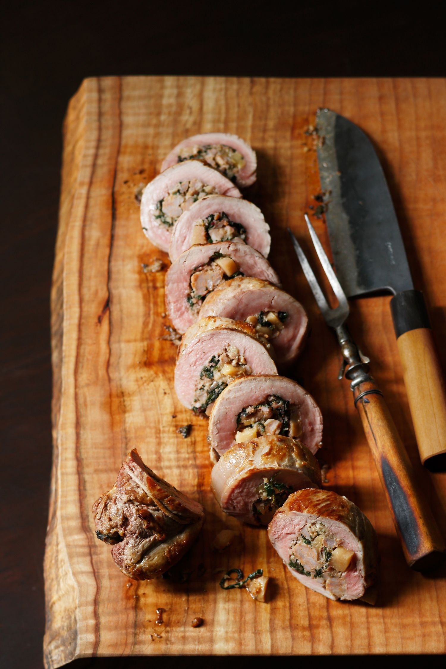 Sliced pork tenderloin stuffed with herbs on a wooden cutting board.