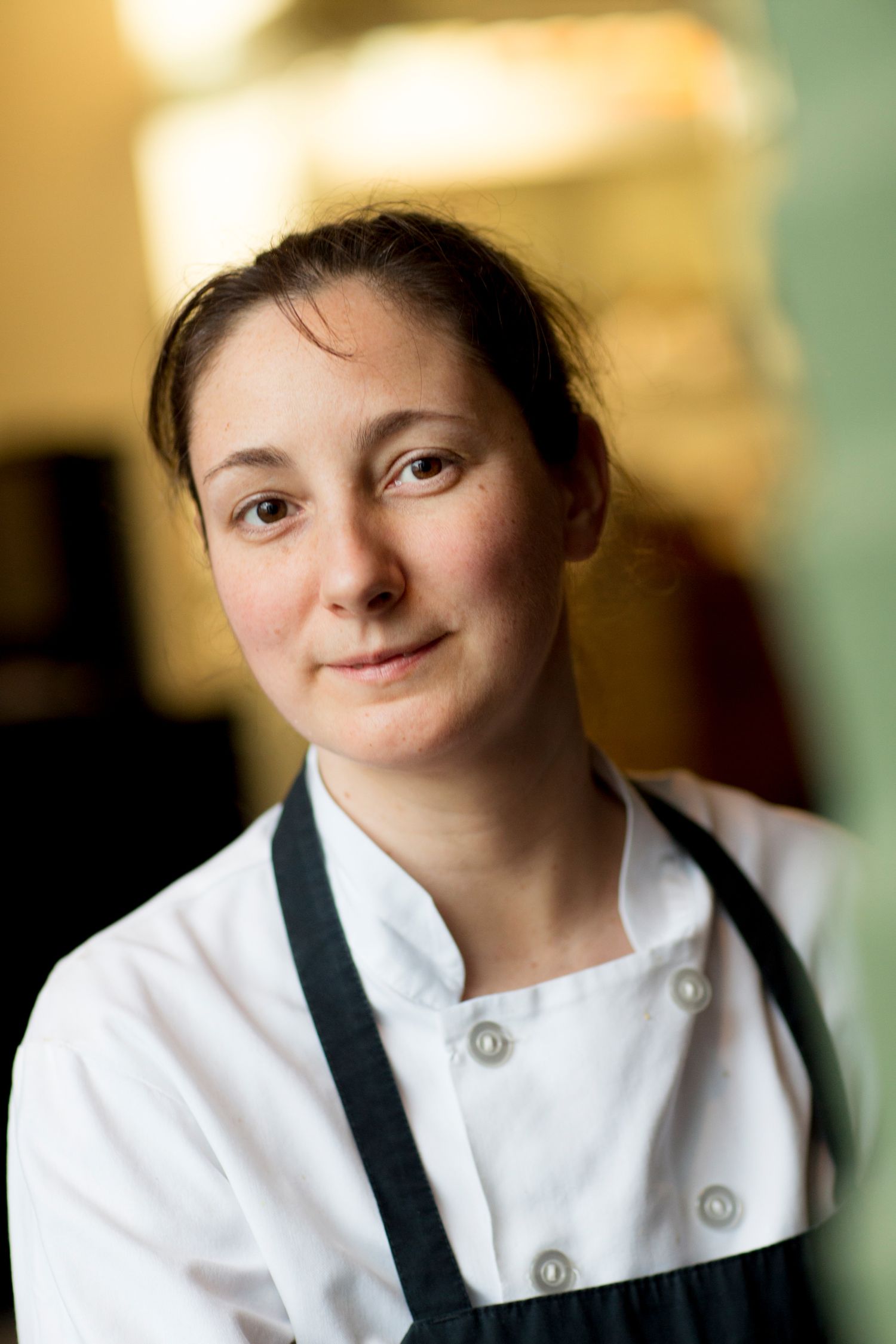 Portrait in warm lighting wearing white chef's coat.