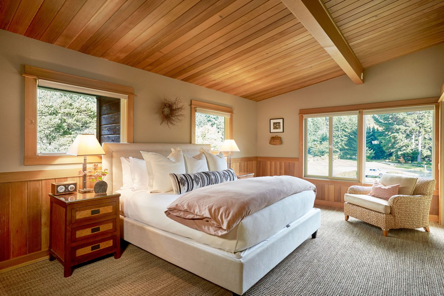 Bright bedroom featuring white bedding, wood ceiling, and multiple windows with natural light.