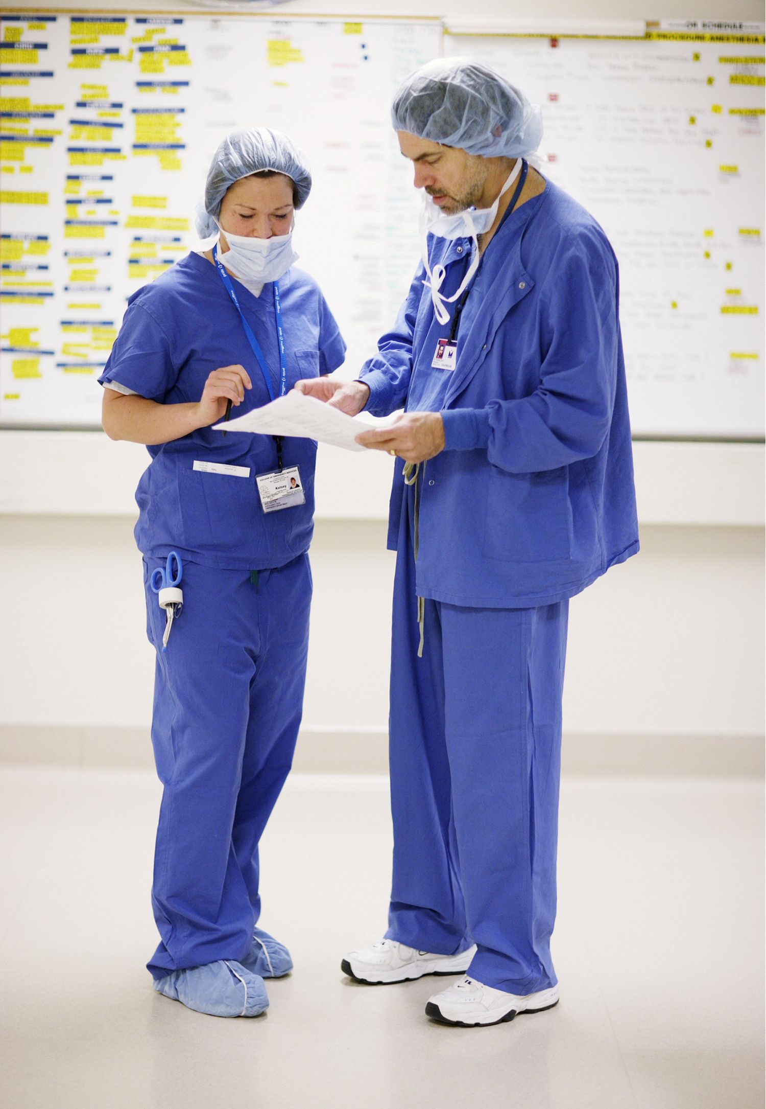 Medical professionals in blue scrubs reviewing patient charts in hospital hallway.