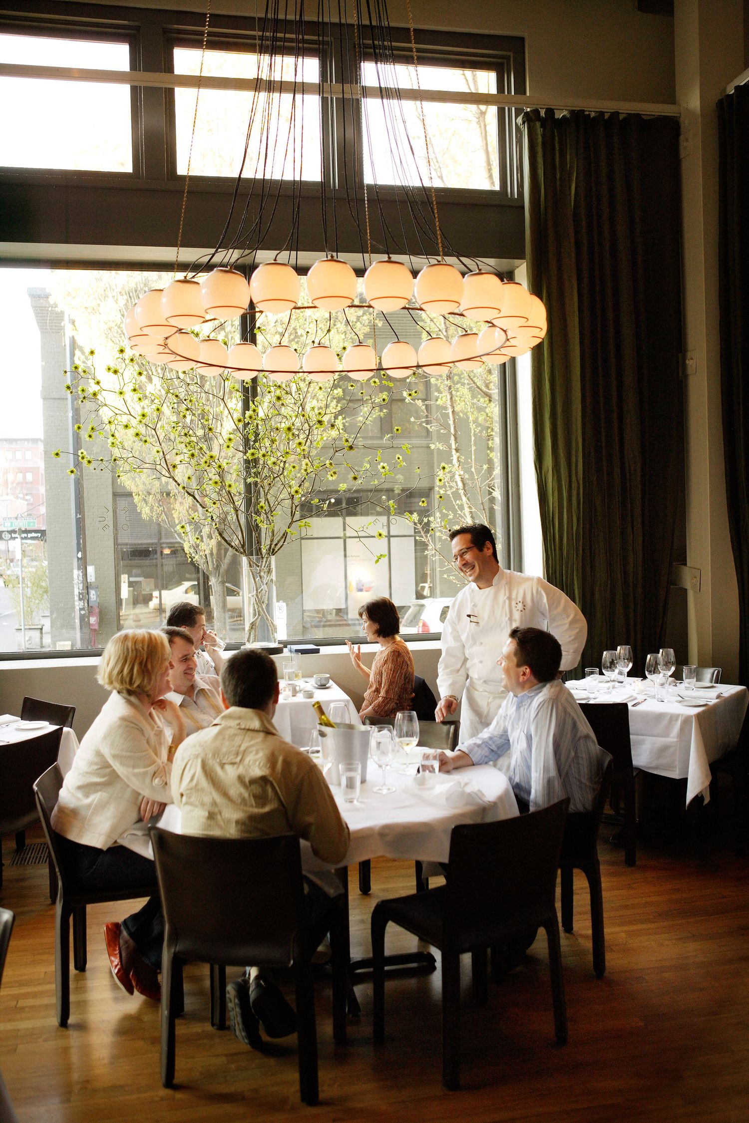 Bright restaurant dining room with white tablecloths and large windows letting in natural light.