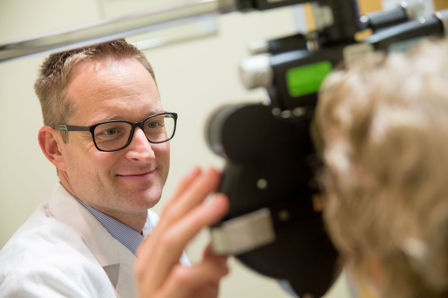 Medical professional using diagnostic equipment in a clinical setting while wearing glasses and a white coat.