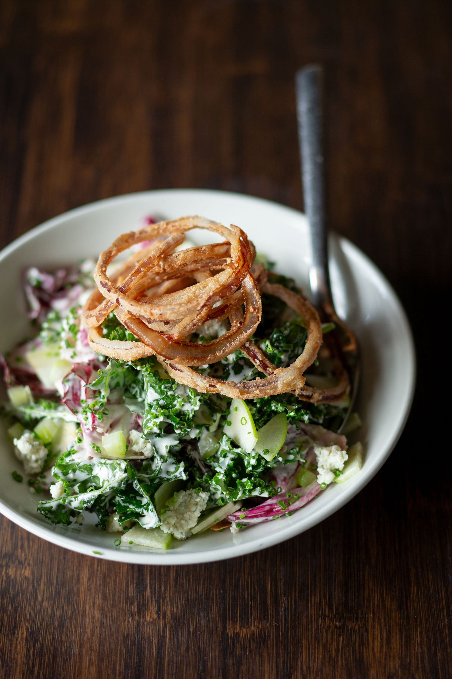 Fresh salad topped with crispy fried onions served on a white plate against dark wood.
