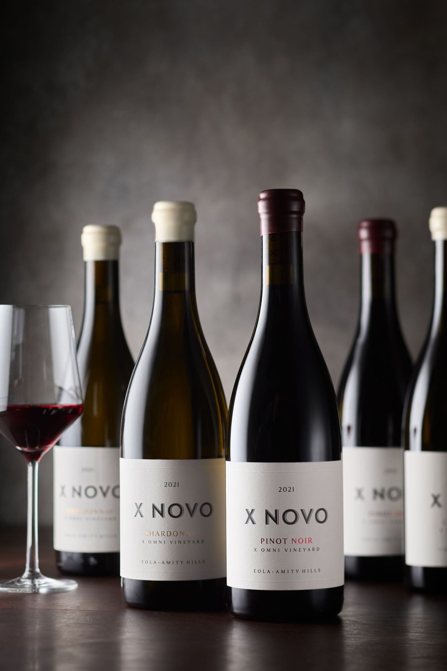 X Novo wine bottles and glasses displayed against a dark dramatic background.