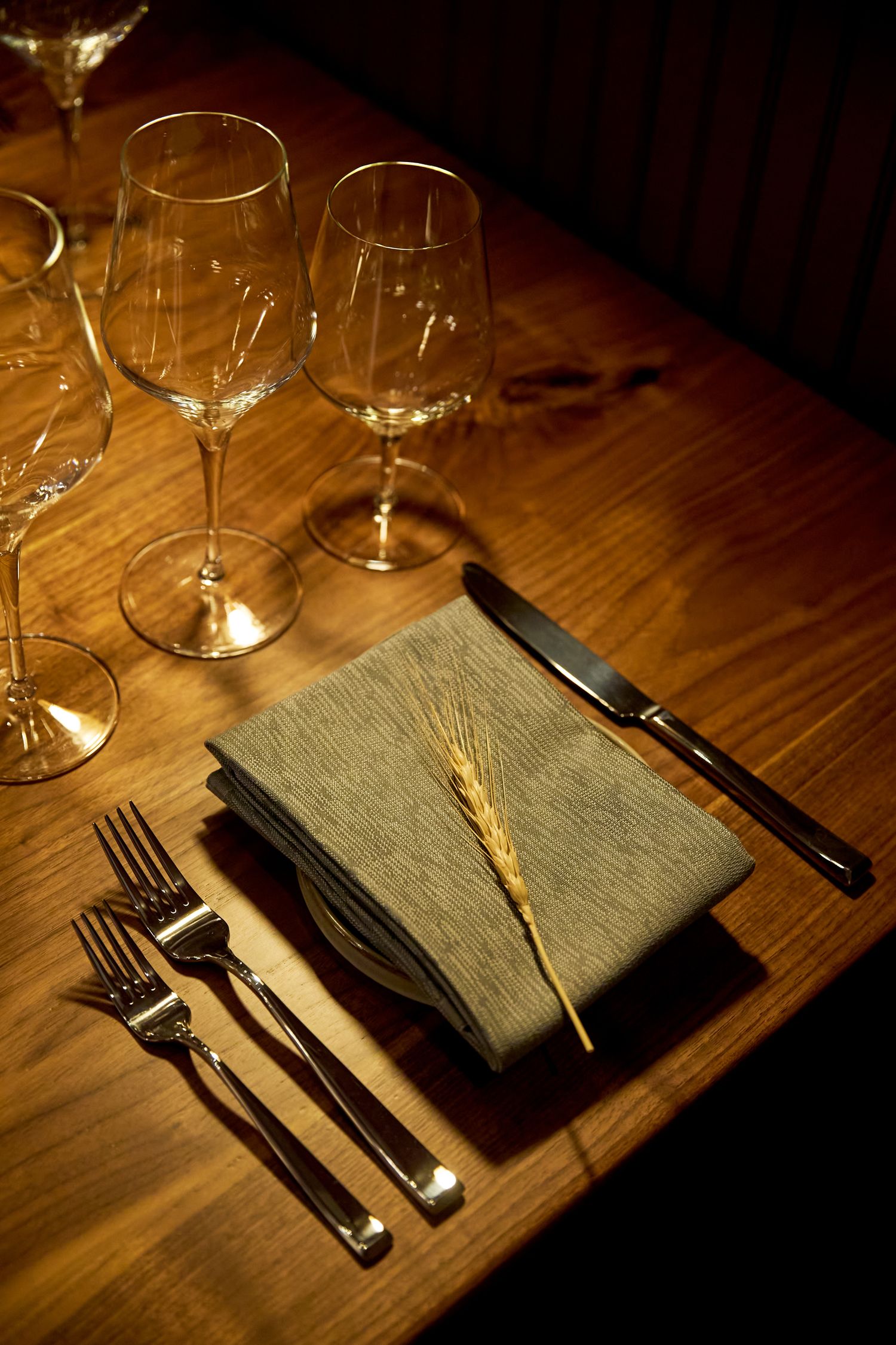 Elegant place setting with wine glasses and silverware on wooden table in warm lighting.