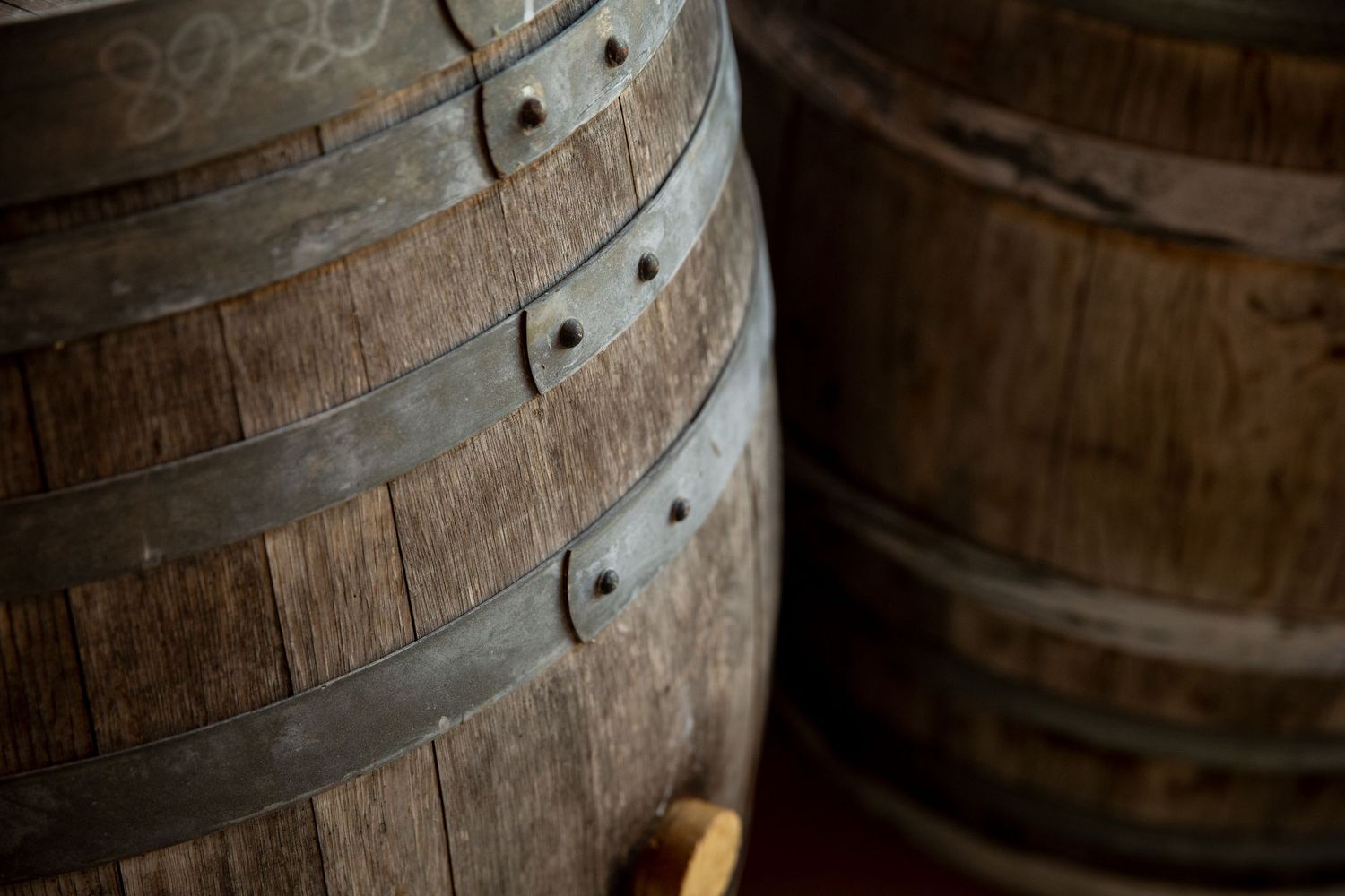 Wooden wine barrels stacked in a dark cellar with dramatic lighting and metal bands around them.