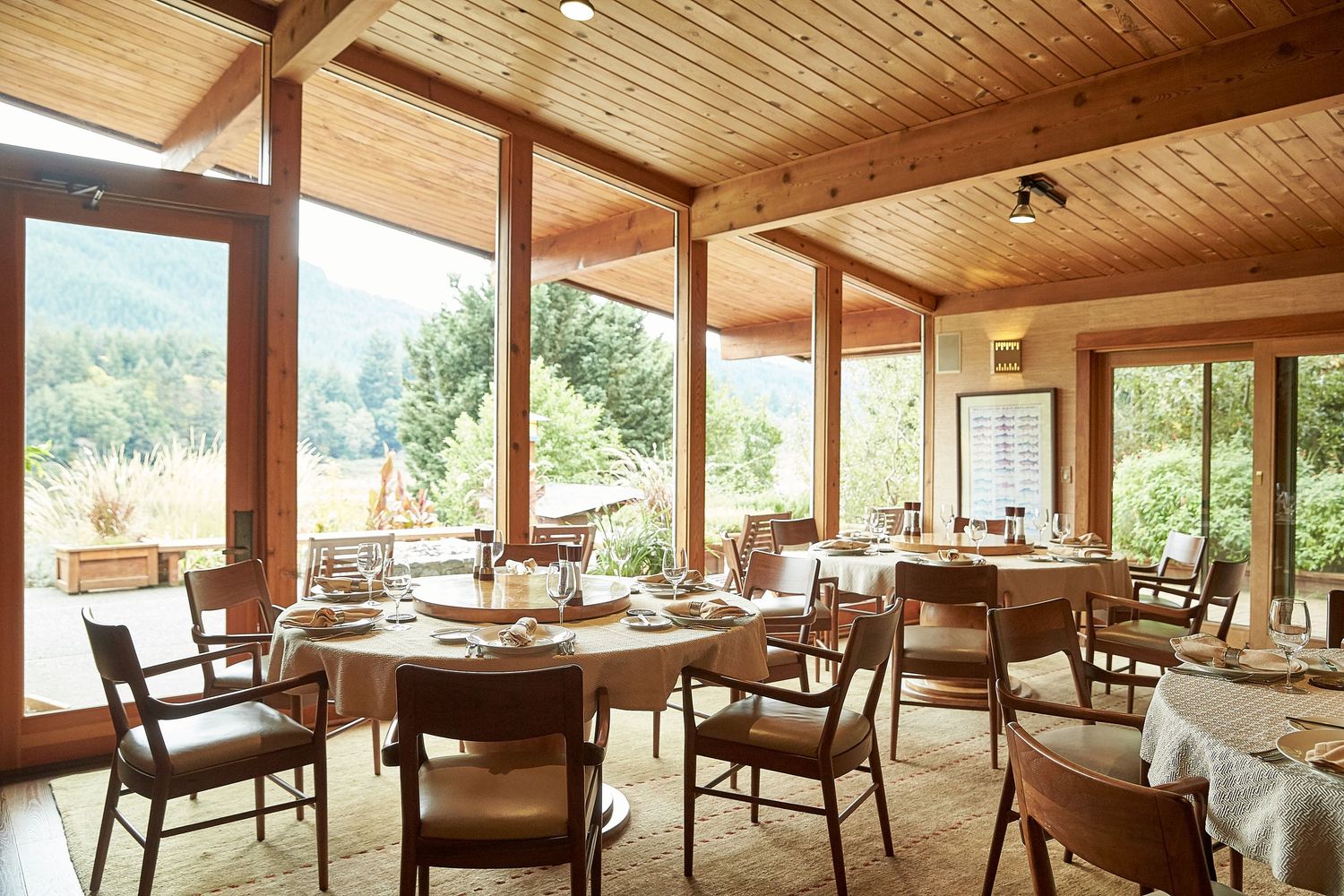 Elegant restaurant dining room with wooden ceiling beams and large windows overlooking natural scenery.