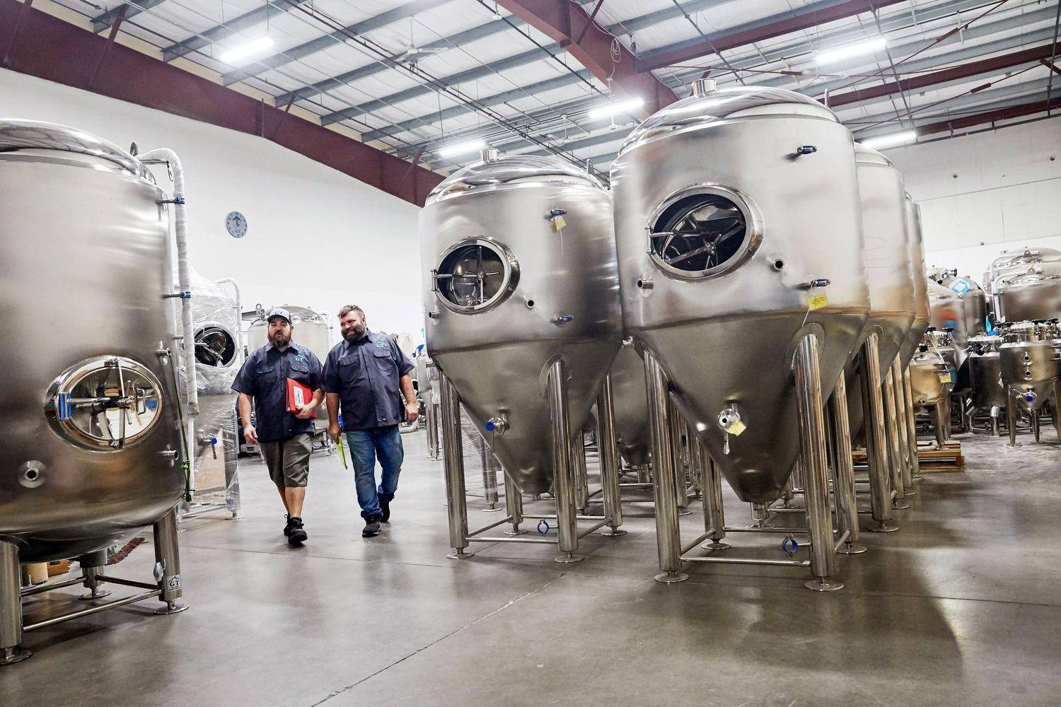Large industrial brewery with stainless steel fermentation tanks in spacious warehouse.