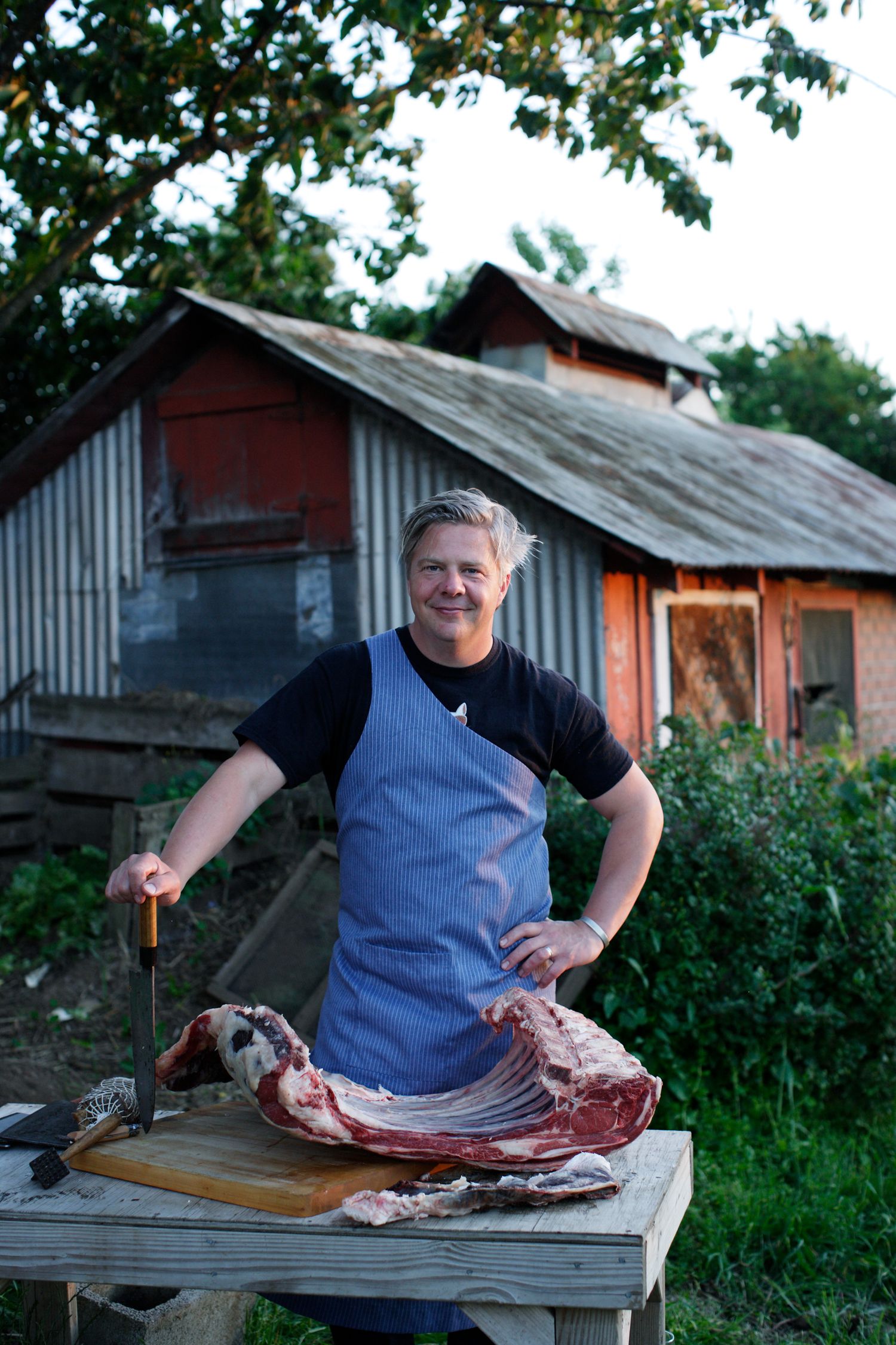 Person preparing meat on wooden table in outdoor rustic setting.
