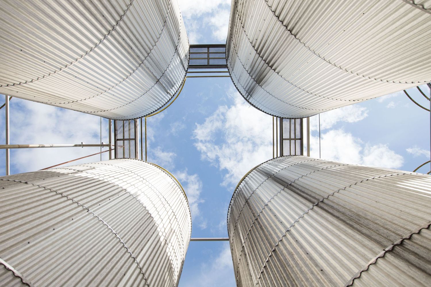 Looking up view of industrial storage silos against blue sky with geometric patterns.