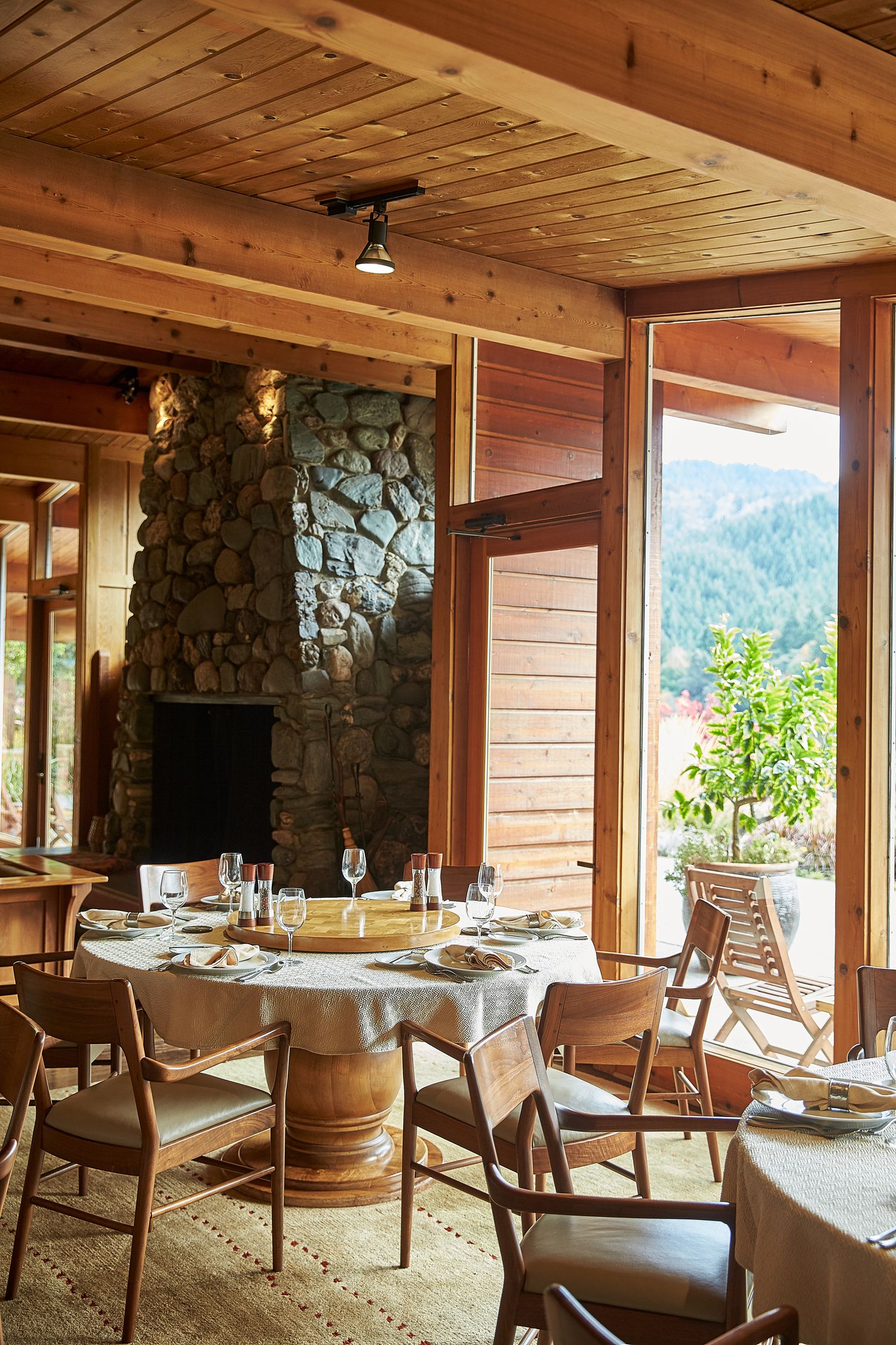 Rustic mountain restaurant interior with wooden beams, stone fireplace and panoramic windows.