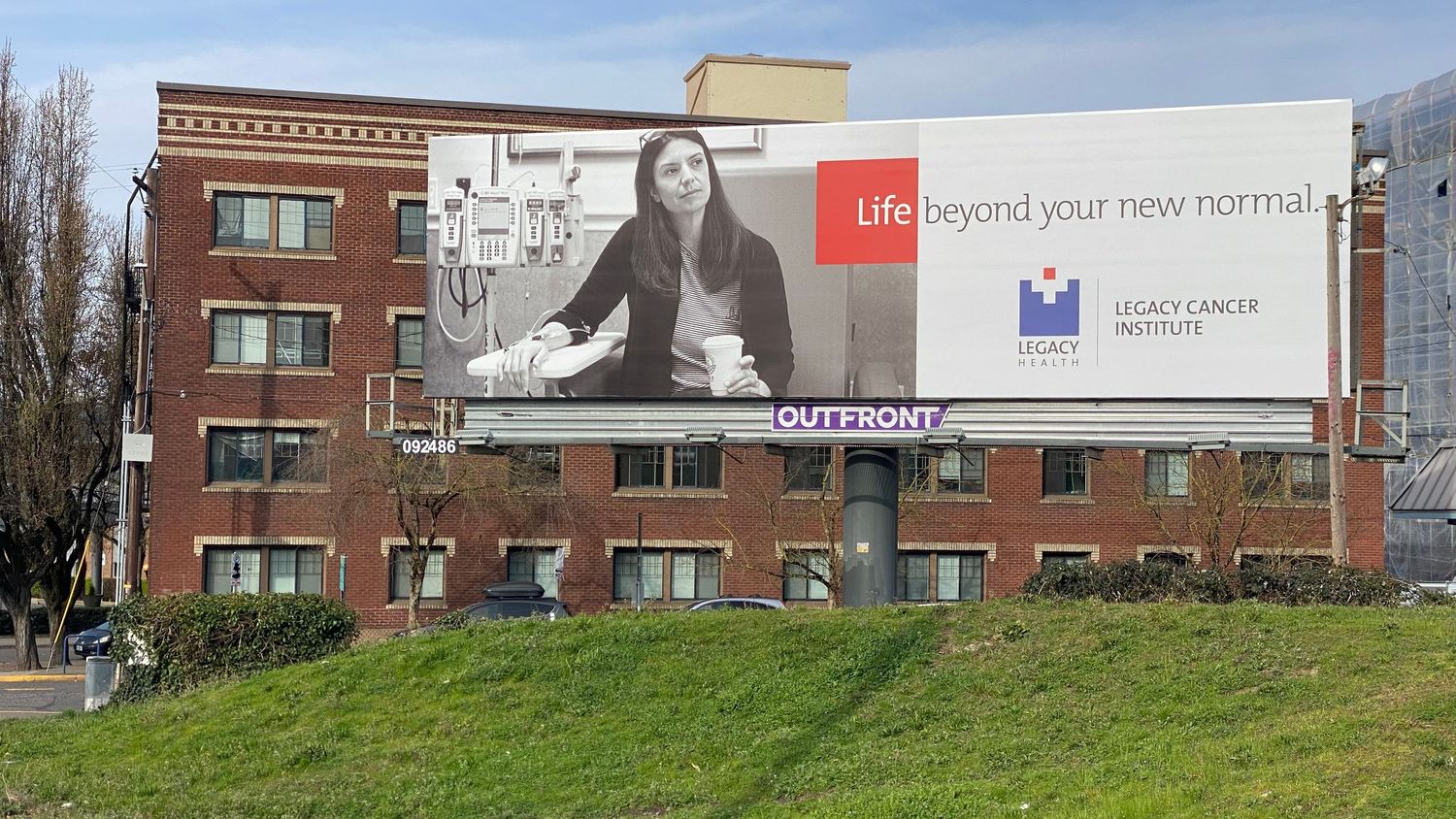Billboard on a brick building showing a woman holding a cup with the text Life beyond your new normal and Legacy Cancer Institute logo.